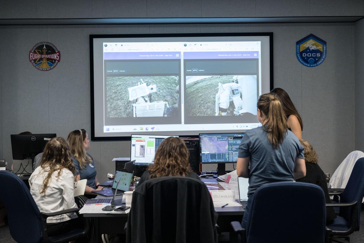 A team of scientists gathered around a table watch video feeds from the cameras worn by NASA astronauts Kate Rubins and Andre Douglas as they performed test moonwalks in the northern Arizona desert while science and flight control teams guided their activities from NASA’s Johnson Space Center in Houston. Credit: NASA/Robert Markowitz