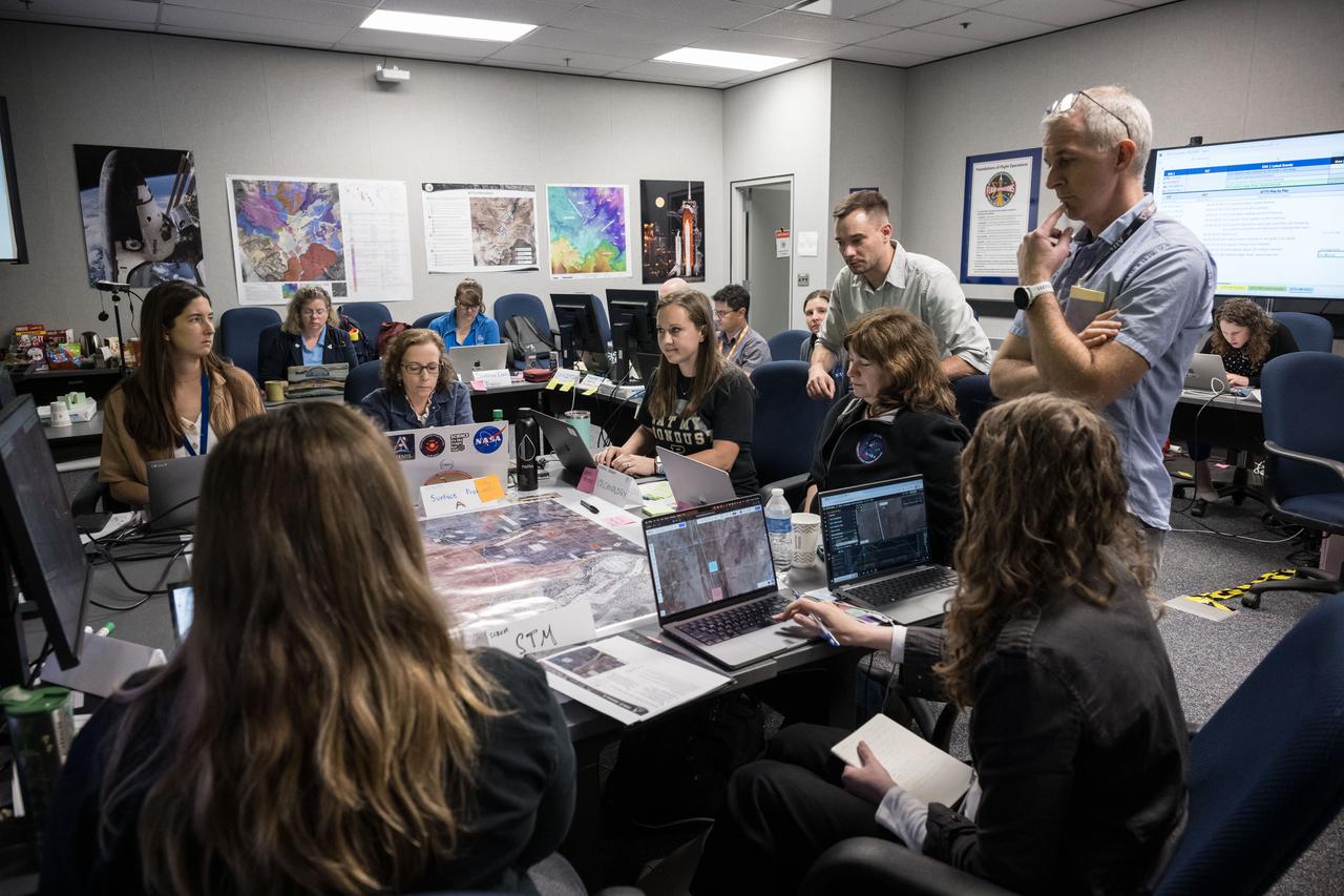 A group of scientists are gathered around a table covered in large maps in the Science Evaluation Room (SER) at NASA’s Johnson Space Center in Houston during the JETT 5 field test. JETT 5 was a week-long field test in the lunar-like landscape of San Francisco Volcanic Field near Flagstaff, Arizona while a team of flight controllers and scientists at Johnson monitor and guide their activities. Credit: NASA/Robert Markowitz