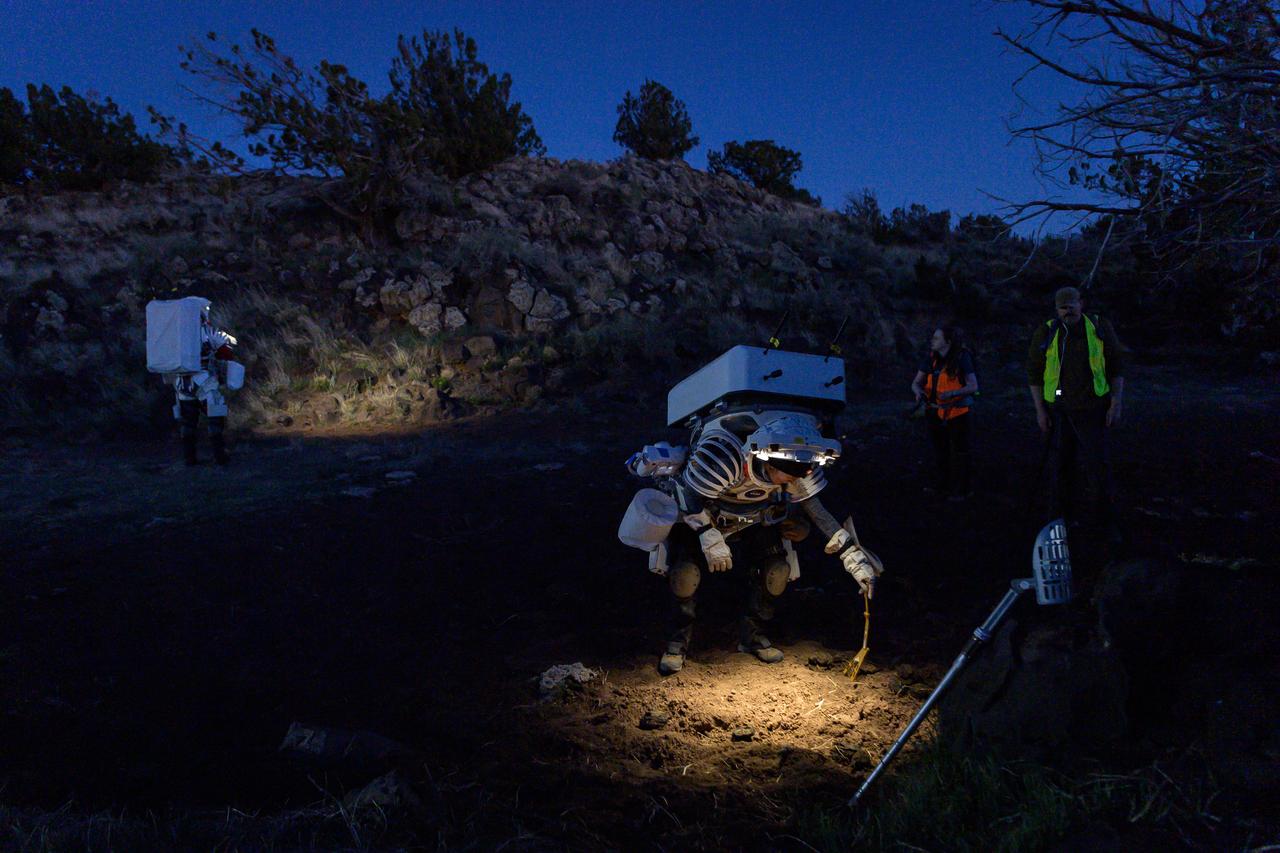 NASA astronaut Kate Rubins places a sample marker in the soil before collecting a sample during a nighttime simulated moonwalk in the San Francisco Volcanic Field in Northern Arizona on May 16, 2024. A sample marker provides a photographic reference point for science samples collected on the lunar surface.  Credit: NASA/Josh Valcarcel 