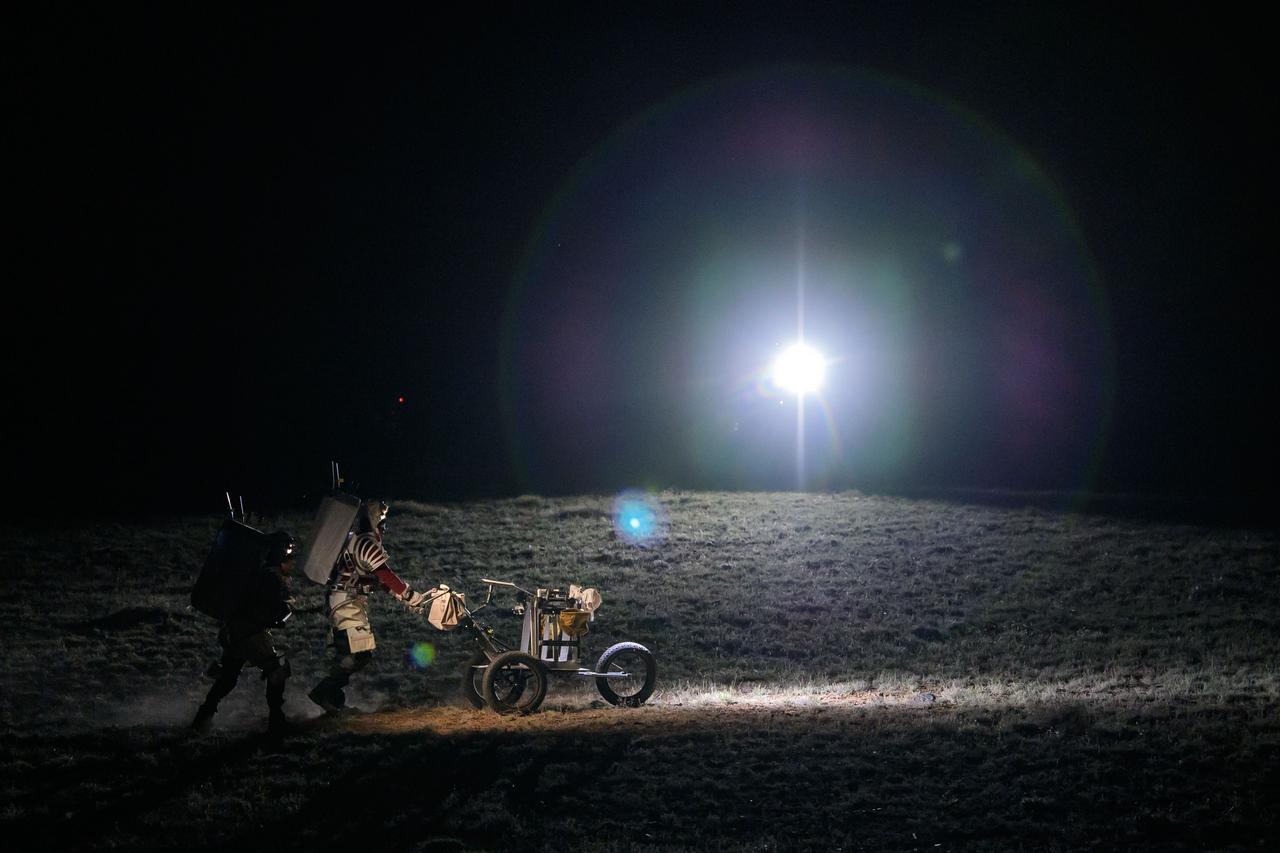 NASA astronaut Andre Douglas pushes a tool cart across the lunar-like landscape while NASA astronaut Kate Rubins follows close behind during a¬¬ nighttime simulated moonwalk in the San Francisco Volcanic Field in Northern Arizona on May 16, 2024.  Credit: NASA/Josh Valcarcel 