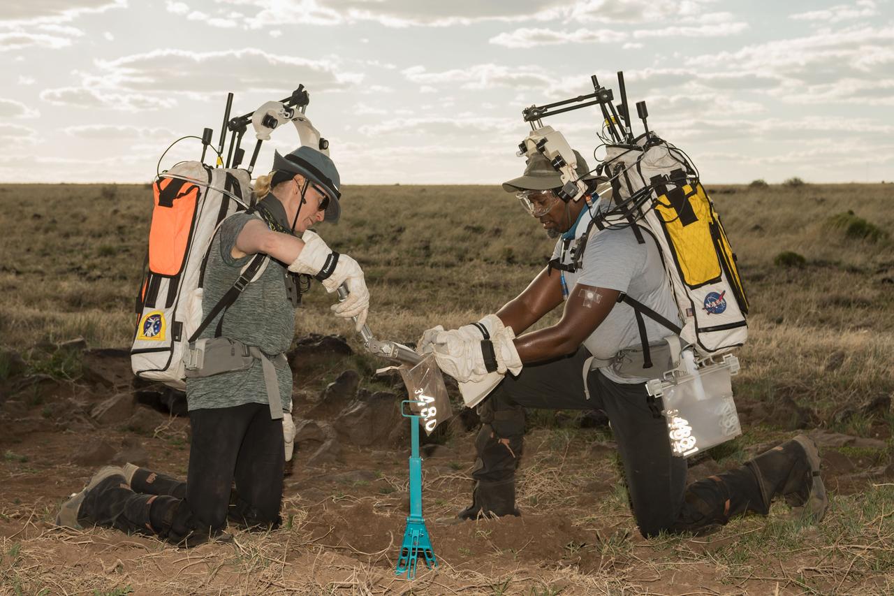 NASA astronaut Andre Douglas holds open a sample bag for NASA astronaut Kate Rubins as she pours some geology samples into it during a simulated moonwalk in the San Francisco Volcanic Field in Northern Arizona on May 17, 2024. Credit: NASA/Josh Valcarcel 
