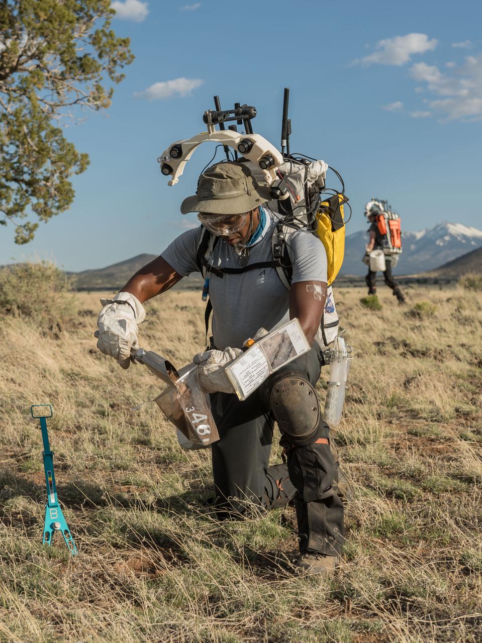 NASA astronaut Andre Douglas pours a scoopful of geologic samples into a sample bag during a simulated moonwalk in the San Francisco Volcanic Field in Northern Arizona on May 17, 2024. Credit: NASA/Josh Valcarcel