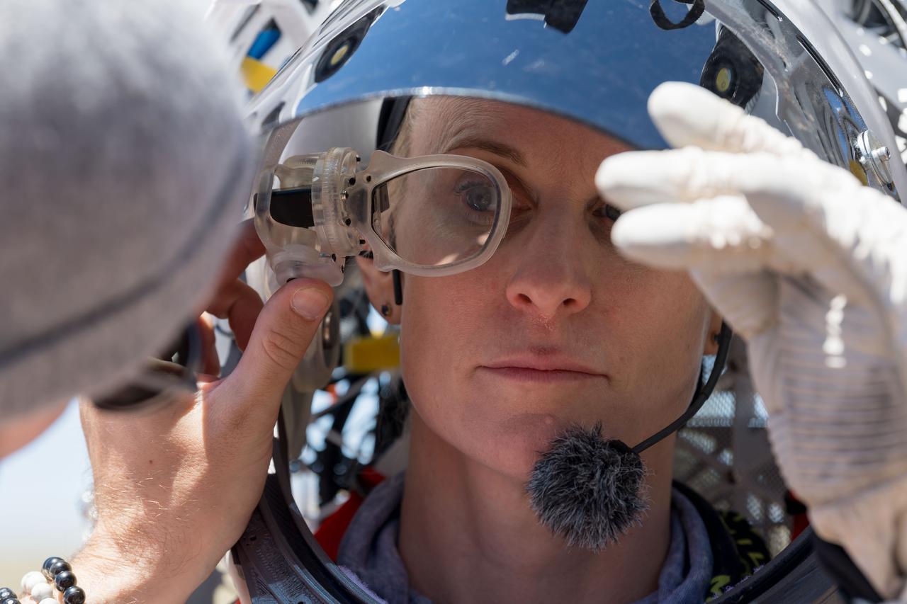 An engineer helps NASA astronaut Kate Rubins adjust the lens on the Joint AR (Joint Augmented Reality Visual Informatics System) display she’s wearing during an advanced technology run in the San Francisco Volcanic Field in Northern Arizona on May 19, 2024. The suit display features include navigation, photo capture, graphical format of consumables, procedure viewing, mission control updates, and other augmented reality cues and graphics. The team successfully tested navigation displays using data from four different data streams: GPS (Global Positioning System)/IMU (Inertial Measurement Unit), camera/IMU, LiDAR (Light Detection and Ranging), and static maps. Technology like this may be used for future Artemis missions to augment mission control communication and help guide crew back to the lunar lander. Credit: NASA/Josh Valcarcel 