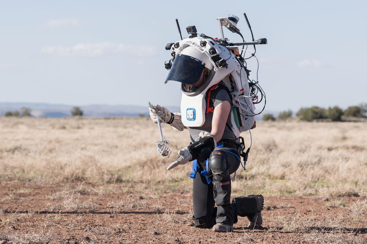 NASA astronaut Kate Rubins uses tongs to pick up a geologic sample while wearing the Joint AR (Joint Augmented Reality Visual Informatics System) display during an advanced technology run in the San Francisco Volcanic Field in Northern Arizona on May 21, 2024. The suit display features include navigation, photo capture, graphical format of consumables, procedure viewing, mission control updates, and other augmented reality cues and graphics. The team successfully tested navigation displays using data from four different data streams: GPS (Global Positioning System)/IMU (Inertial Measurement Unit), camera/IMU, LiDAR (Light Detection and Ranging), and static maps. Technology like this may be used for future Artemis missions to augment mission control communication and help guide crew back to the lunar lander. Credit: NASA/Josh Valcarcel 