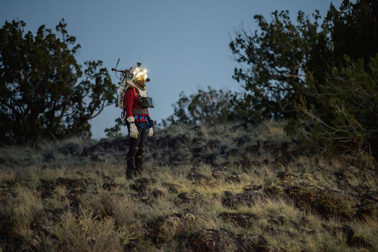 NASA astronaut Andre Douglas views the lunar-like landscape at dusk while wearing the Joint AR (Joint Augmented Reality Visual Informatics System) display during an advanced technology run in the San Francisco Volcanic Field in Northern Arizona on May 21, 2024. The suit display features include navigation, photo capture, graphical format of consumables, procedure viewing, mission control updates, and other augmented reality cues and graphics. The team successfully tested navigation displays using data from four different data streams: GPS (Global Positioning System)/IMU (Inertial Measurement Unit), camera/IMU, LiDAR (Light Detection and Ranging), and static maps. Technology like this may be used for future Artemis missions to augment mission control communication and help guide crew back to the lunar lander. Credit: NASA/Josh Valcarcel 