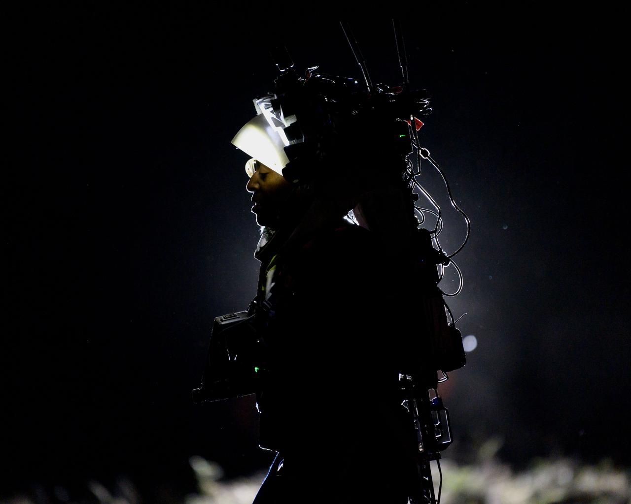 NASA astronaut Andre Douglas wears  the Joint AR (Joint Augmented Reality Visual Informatics System) display during a nighttime advanced technology run in the San Francisco Volcanic Field in Northern Arizona on May 21, 2024. The suit display features include navigation, photo capture, graphical format of consumables, procedure viewing, mission control updates, and other augmented reality cues and graphics. The team successfully tested navigation displays using data from four different data streams: GPS (Global Positioning System)/IMU (Inertial Measurement Unit), camera/IMU, LiDAR (Light Detection and Ranging), and static maps. Technology like this may be used for future Artemis missions to augment mission control communication and help guide crew back to the lunar lander. Credit: NASA/Josh Valcarcel 