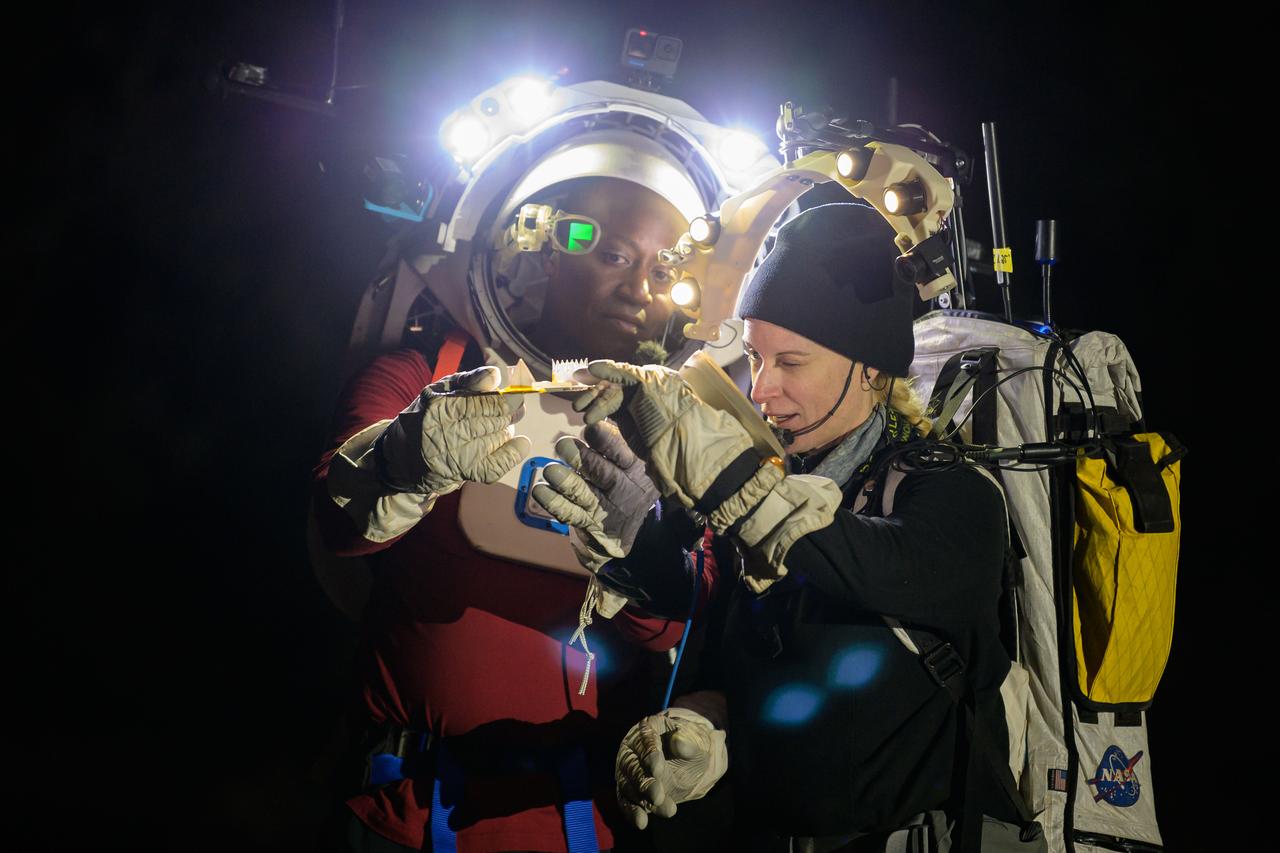 NASA astronauts Andre Douglas and Kate Rubins during a nighttime advanced technology run in the San Francisco Volcanic Field in Northern Arizona on May 21, 2024. Douglas is wearing the Joint AR (Joint Augmented Reality Visual Informatics System) display. The suit display features include navigation, photo capture, graphical format of consumables, procedure viewing, mission control updates, and other augmented reality cues and graphics. The team successfully tested navigation displays using data from four different data streams: GPS (Global Positioning System)/IMU (Inertial Measurement Unit), camera/IMU, LiDAR (Light Detection and Ranging), and static maps. Technology like this may be used for future Artemis missions to augment mission control communication and help guide crew back to the lunar lander. Credit: NASA/Josh Valcarcel
