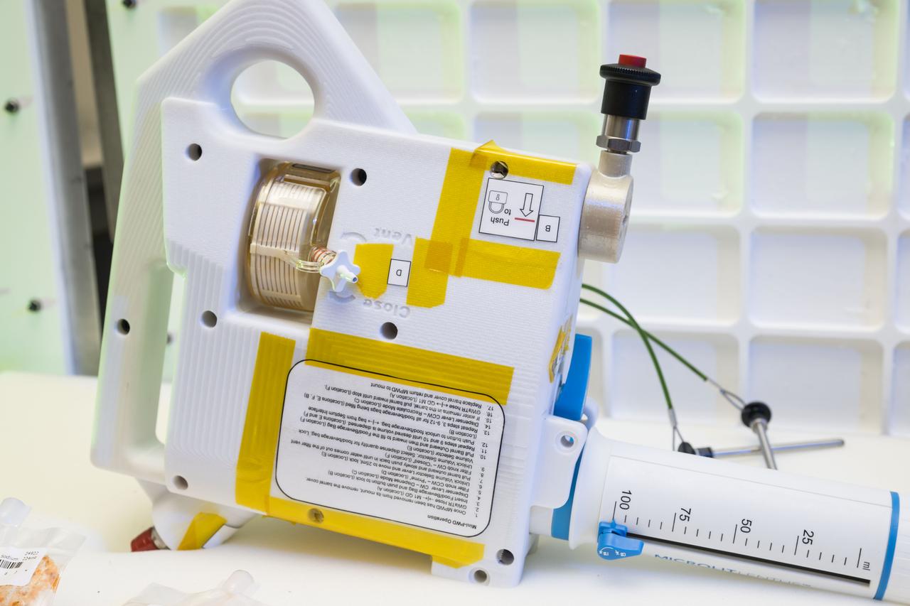 jsc2024e040691 -- A prototype of the Mini Potable Water Dispenser, currently in development at NASA’s Marshall Space Flight Center, is displayed alongside various food pouches during a demonstration at NASA’s Johnson Space Center. Photo Credit: NASA/David DeHoyos