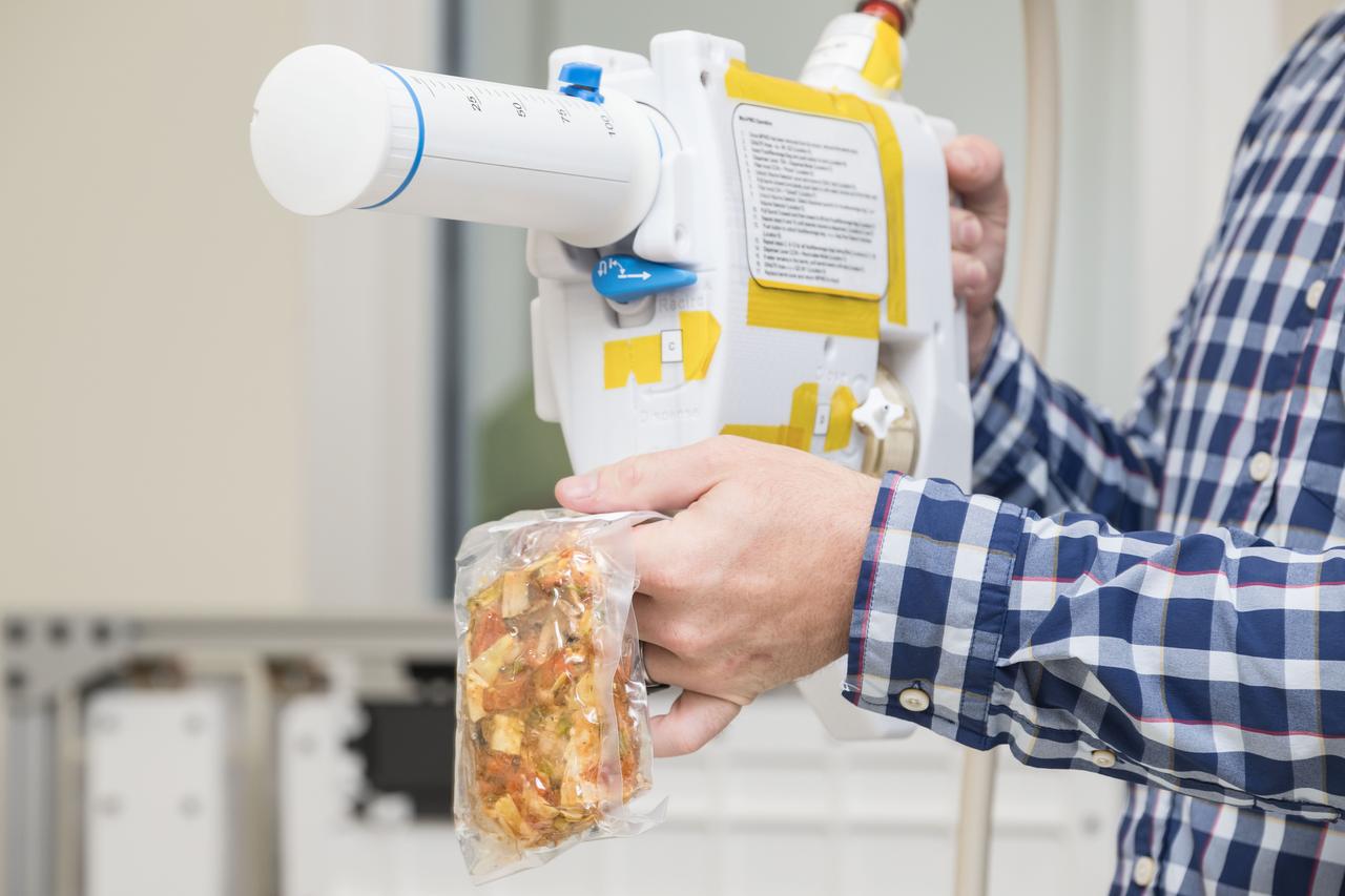 jsc2024e040708 -- An engineer demonstrates the use of the Mini Potable Water Dispenser by rehydrating a food pouch during a testing session at Johnson Space Center on June 6, 2024. This compact, lightweight dispenser is designed to help astronauts prepare meals in deep space. Photo Credit:  NASA/David DeHoyos