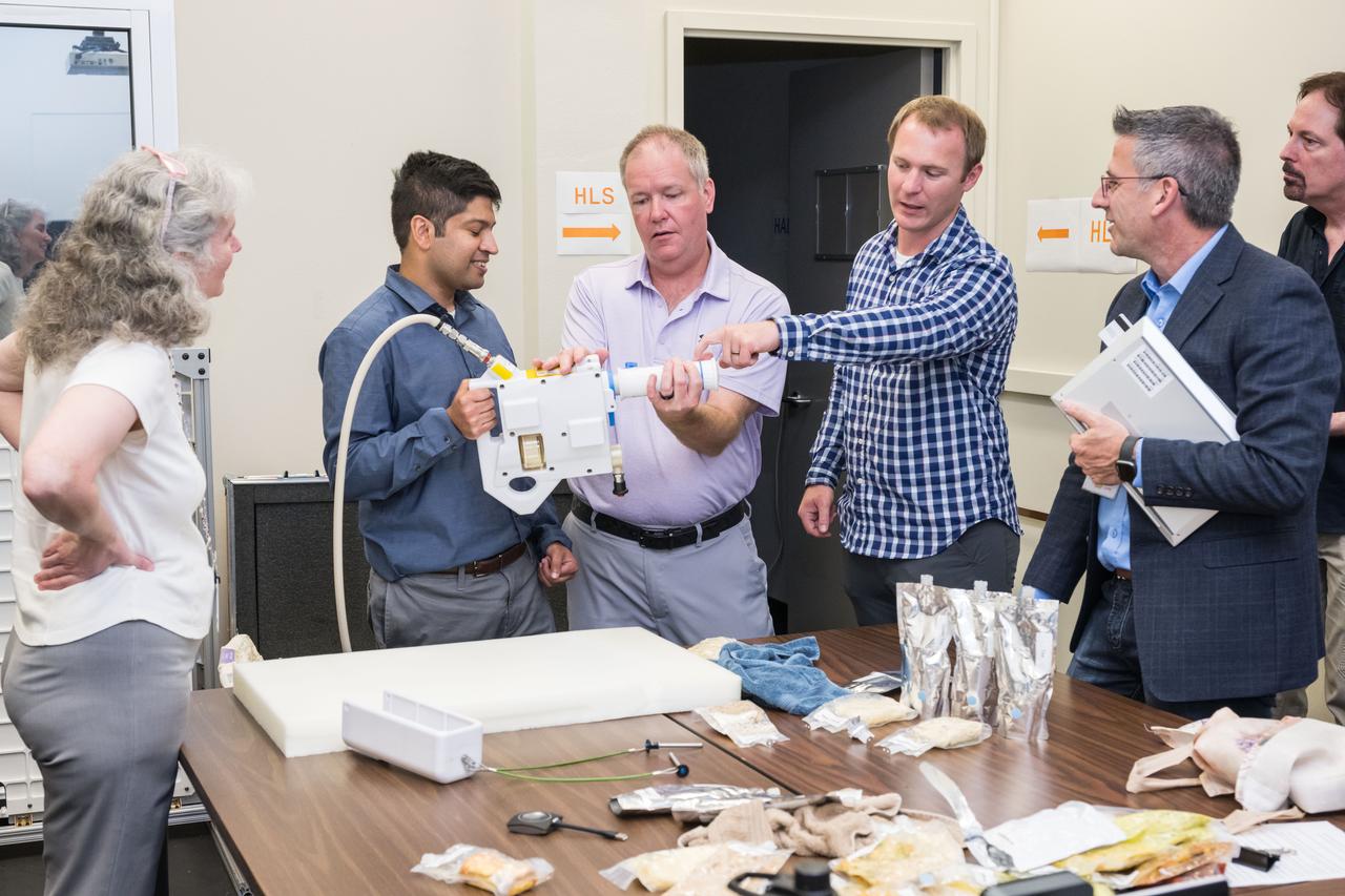 jsc2024e040779 -- Project manager Shaun Glasgow (middle) demonstrates the Mini Potable Water Dispenser during a testing session at NASA's Johnson Space Center. Photo Credit:  NASA/David DeHoyos