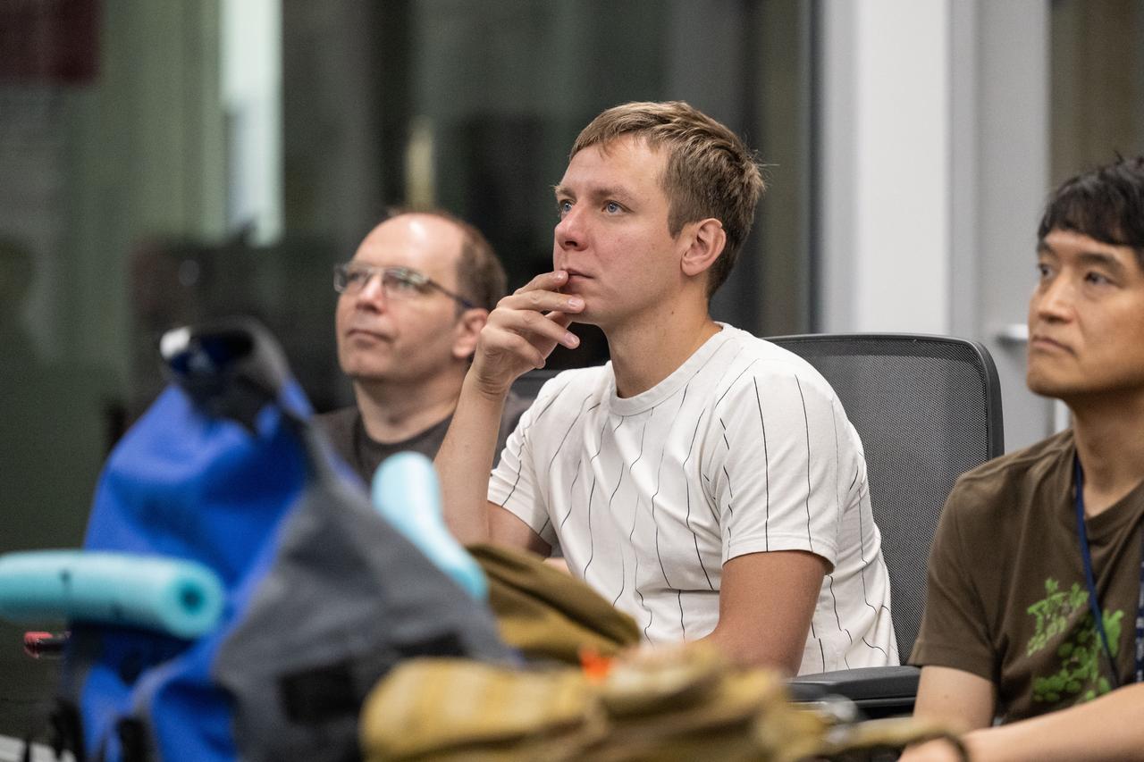 jsc2023e040978 (June 7, 2024) --- (From left) A mission trainer and SpaceX Crew-10 Mission Specialists Kirill Peskov of Roscosmos and Takuya Onishi of JAXA (Japan Aerospace Exploration Agency) watch a demonstration before water survival training in the Neutral Buoyancy Laboratory at NASA's Johnson Space Center.