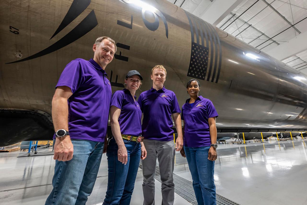 jsc2024e050140 (May 13, 2024) --- NASA’s SpaceX Crew-9 members stand in front of a Falcon 9 first-stage booster at SpaceX’s HangarX facility at NASA's Kennedy Space Center in Florida.  From left are, Pilot Nick Hague from NASA; Commander Zena Cardman from NASA; Mission Spedialist Alexsandr Gorbunov from Roscosmos; and Mission Specialist Stephanie Wilson from NASA. Credit: SpaceX