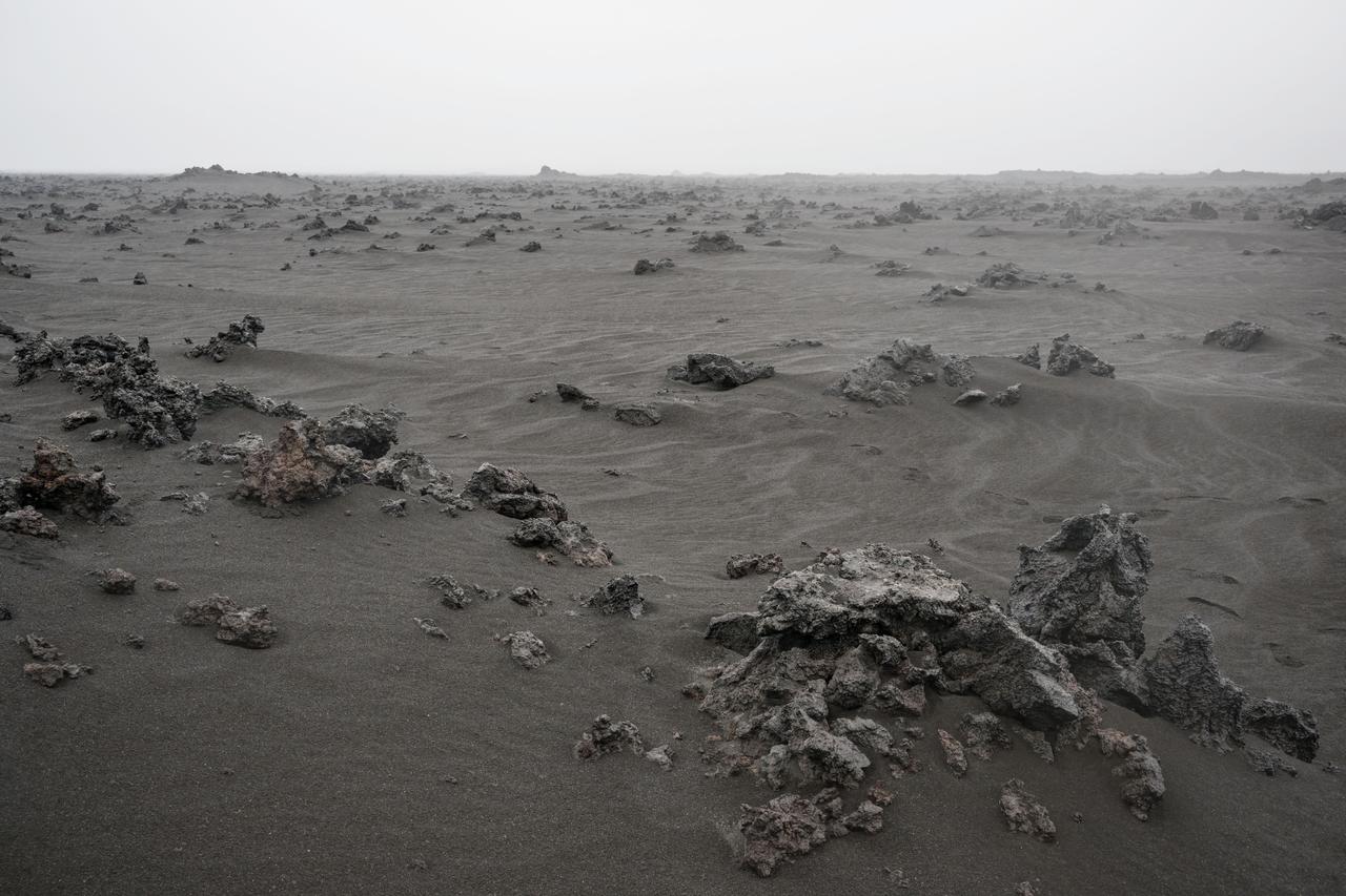 A view of the Holuhraun lava field from the Bárðarbunga volcano, located in Vatnajökull National Park in Iceland. The image shows the rubbly textured basaltic lava flow that has been partially buried by wind-blown sediment. Iceland has been used as a planetary analog for geology training for astronauts since the Apollo missions because of the geologic similarities to the Moon. 