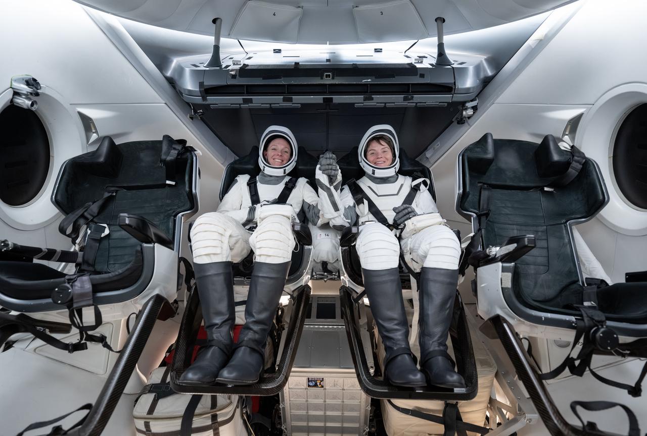 jsc2024e066393 (Sept. 26, 2024) --- NASA astronauts (from left) Nichole Ayers and Anne McClain, NASA's SpaceX Crew-10 mission pilot and commander respectively, smile and grab hands during a simulation inside a mockup of a Dragon cockpit at the company's facilities in Hawthorne, California. Credit: SpaceX