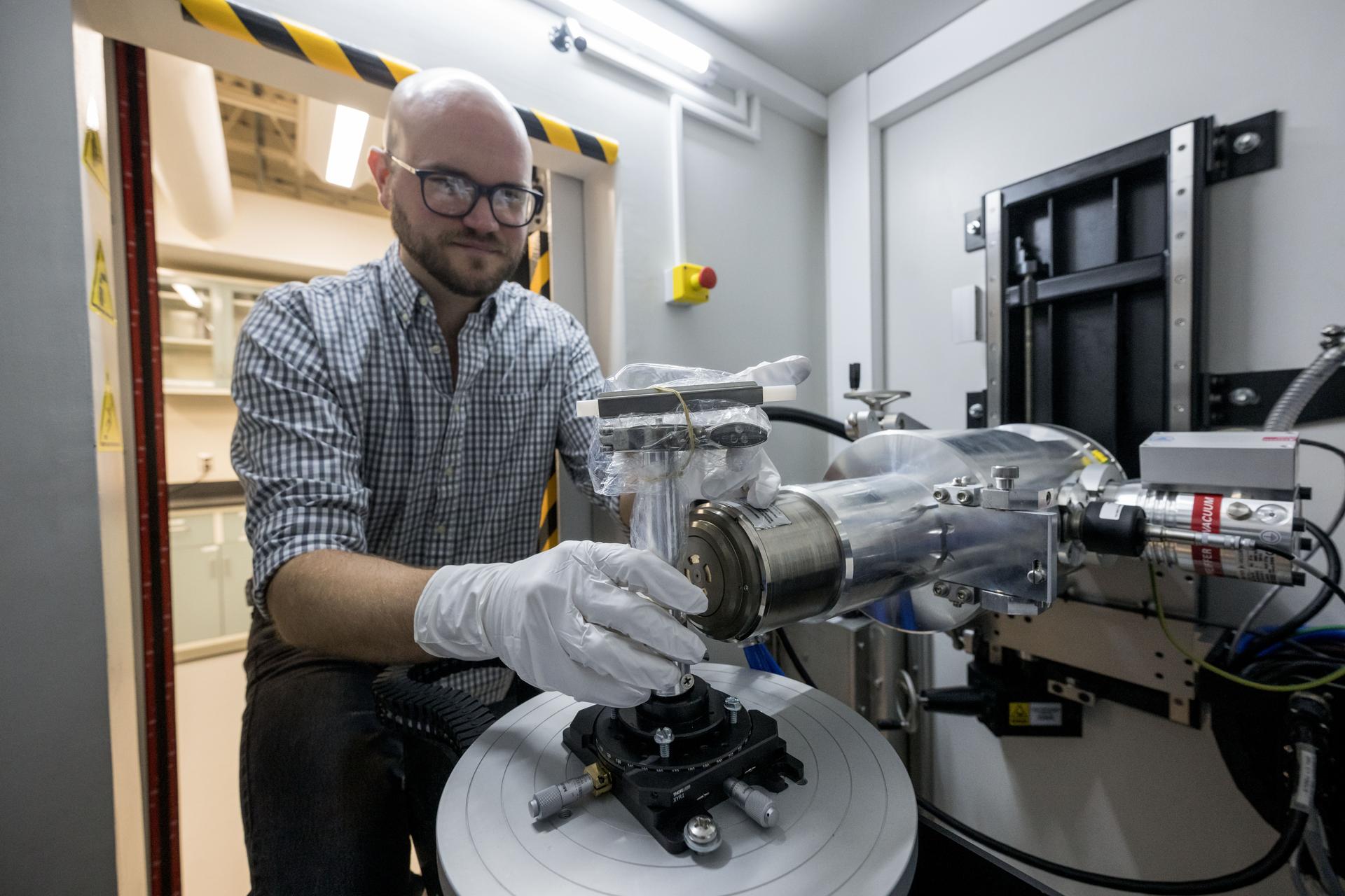 jsc2024e076997 --- Scott Eckley, X-ray scientist within NASA Johnson Space Center’s Astromaterials Research and Exploration Science (ARES), demonstrates the process for placing a container holding a piece of asteroid material in an X-Ray Computed Tomography (XCT) machine. XCT scans let researchers image particles through airtight containers and visualize a rock’s shape and internal structure without damaging the sample. Credit: NASA/Robert Markowitz