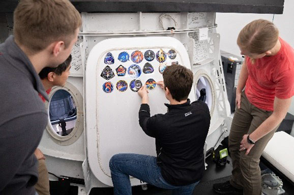 NASA astronaut and commander of NASA's SpaceX Crew-10 mission Anne McClain places the Crew-10 mission patch sticker on the Dragon training hatch at the company’s facility in Hawthorne, California.