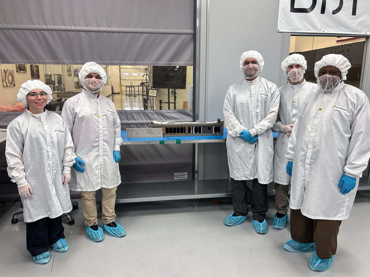 jsc2025e039328 (3/17/2025) --- The EagleSat integration team poses for one last photo with EagleSat-2. Memory Degradation Experiment (NanoRacks-EagleSat-2) documents the effects of solar radiation on five types of commercially available computer memory devices. Results from this investigation could help the space community better prepare for, remediate, and even avoid data memory loss from satellites in orbit. Imagery courtesy of EagleSat-2 Team.