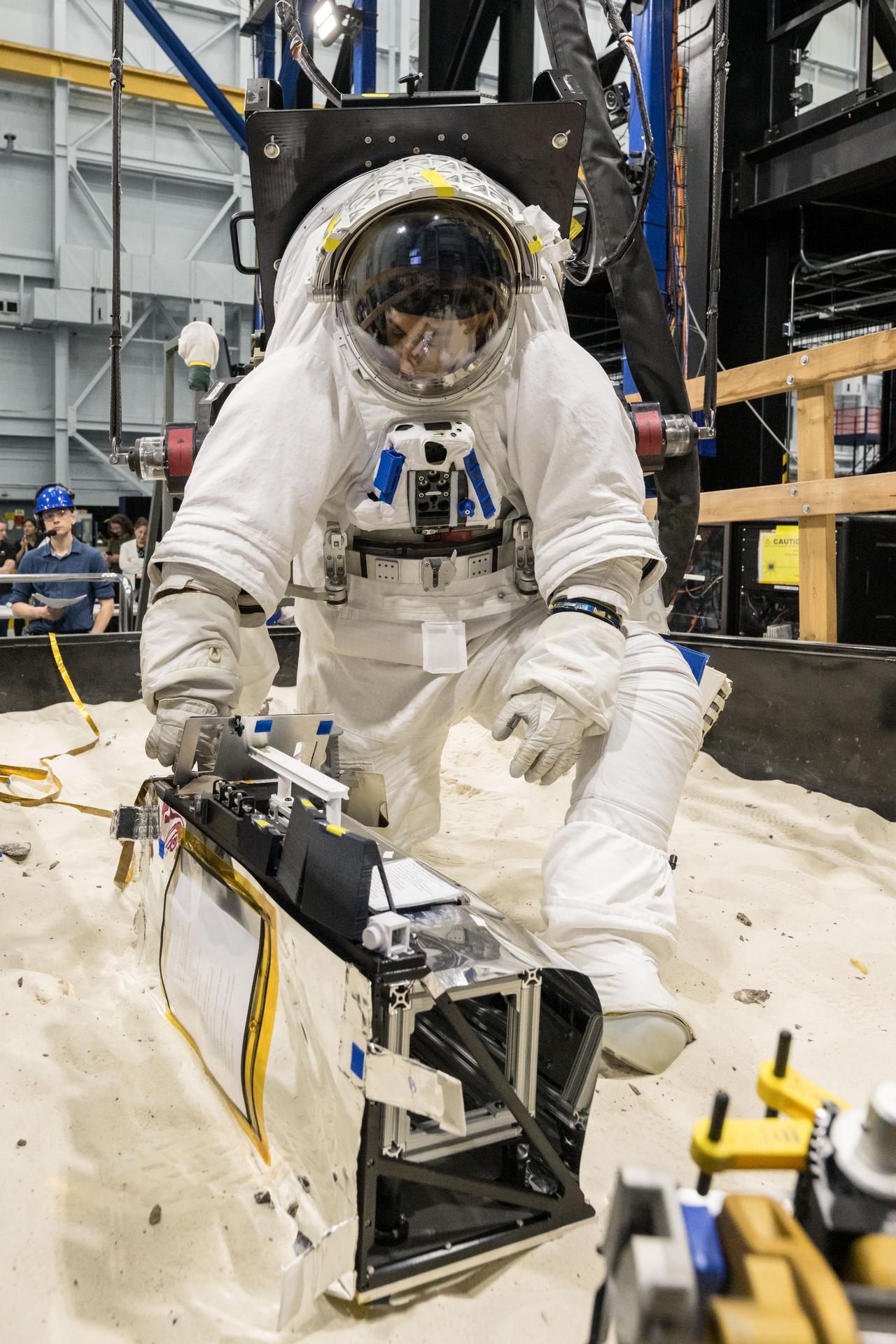 Trevor Graff, the Artemis Science Team Hardware and Testing Lead, deploys a mockup of the Lunar Environment Monitoring Station (LEMS) during testing with the Active Response Gravity Offload System (ARGOS) at Johnson Space Center in Houston, Texas on April 21st, 2025. LEMS is a compact, autonomous, and self-sustaining seismometer suite designed to carry out continuous, long-term, monitoring of the lunar seismic environment at the South Polar region. Photo Credit: NASA/ James Blair