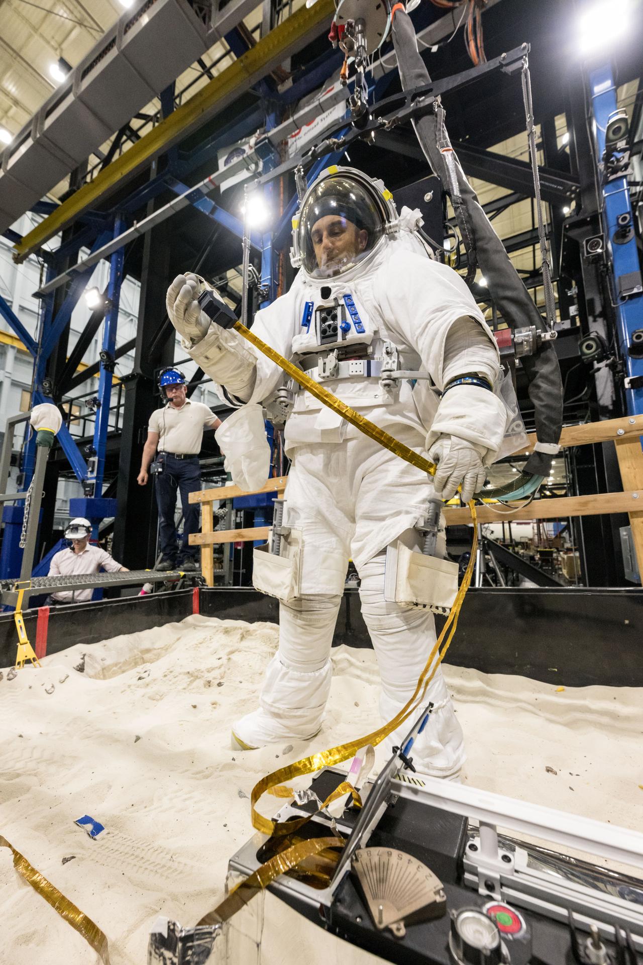 Trevor Graff, the Artemis Science Team Hardware and Testing Lead, deploys a mockup of the Lunar Environment Monitoring Station (LEMS) during testing with the Active Response Gravity Offload System (ARGOS) at Johnson Space Center in Houston, Texas on April 21st, 2025. LEMS is a compact, autonomous, and self-sustaining seismometer suite designed to carry out continuous, long-term, monitoring of the lunar seismic environment at the South Polar region. Photo Credit: NASA/ James Blair