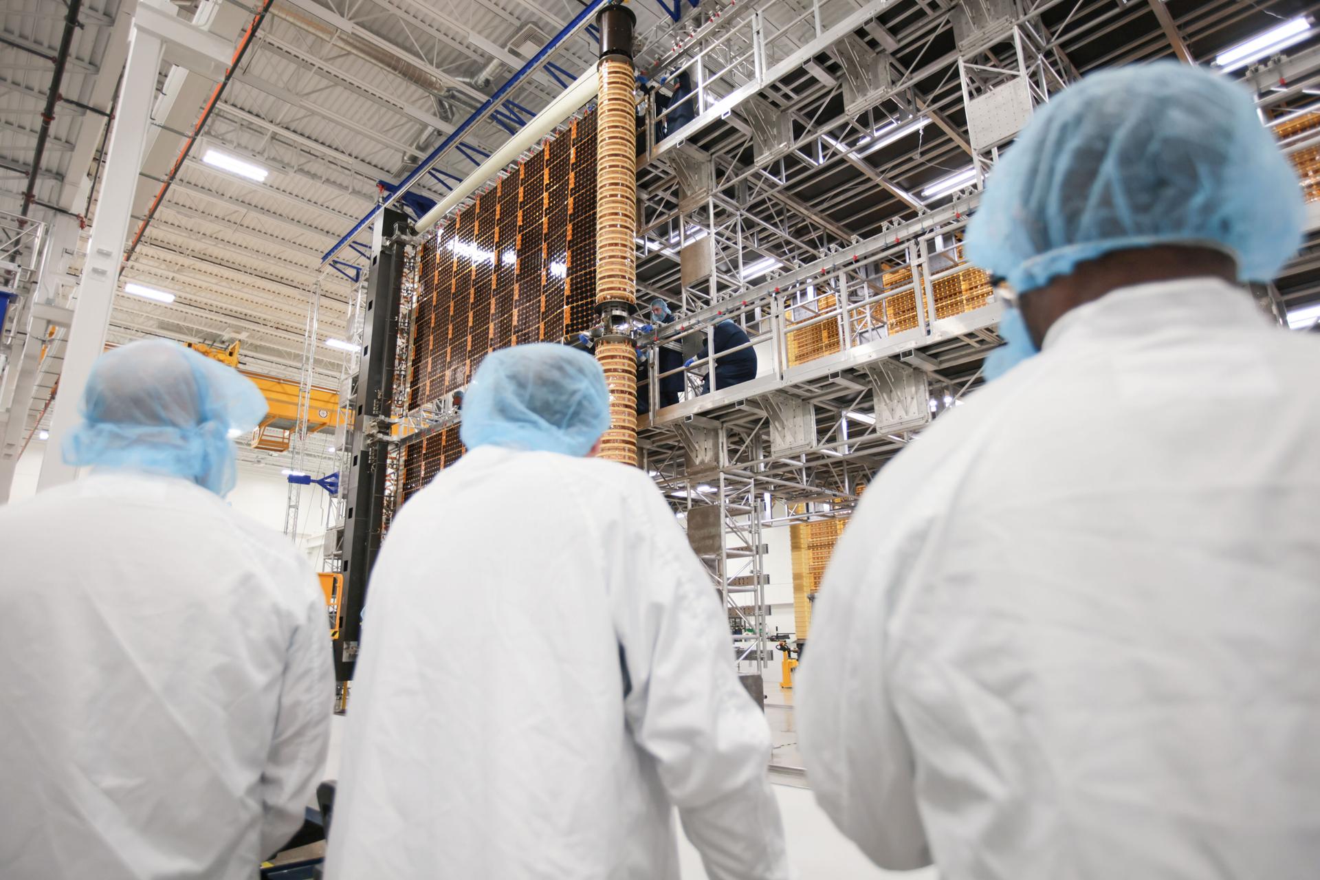 NASA and industry team members observe a Roll-Out Solar Array (ROSA) wing for Gateway as it deploys inside Redwire’s high-bay facility in Goleta, California, during a test on June 30, 2025. The image shows the solar array partially extended as technicians monitor the process from the facility floor and elevated work platforms. Credit: Lanteris Space Systems