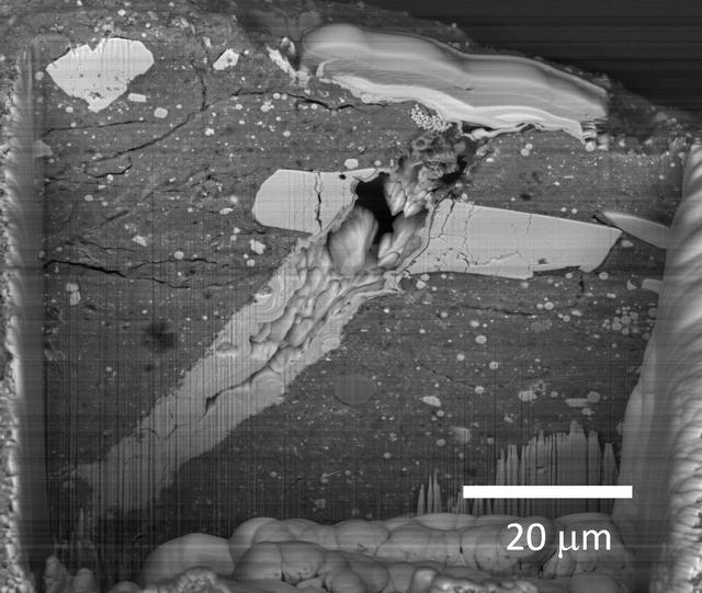 A scanning electron microscope image of a micrometeorite impact crater in a particle of asteroid Bennu material. Scientists found microscopic craters and tiny splashes of once-molten rock – known as impact melts – on the surfaces of samples, signs that the asteroid was bombarded by micrometeorites.