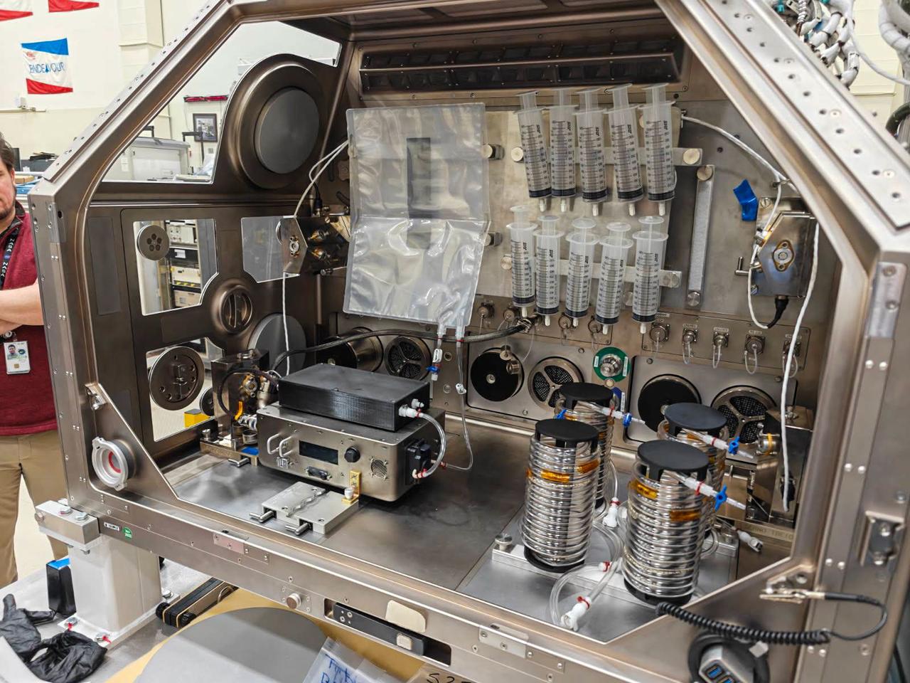 NASA Image: JSC2026E004232 - Intravenous Fluid Generation – Mini (IVGEN Mini) hardware inside the Life Sciences Glovebox (LSG) ground facility at Marshall Space Flight Center (MSFC). IVGEN Mini aims to verify operations for a miniaturized system and its ability to make medical-grade saline solution using potable water aboard the International Space Station. On future exploration missions, this system could give crew members the ability to generate intravenous fluids on demand. Credit: NASA.