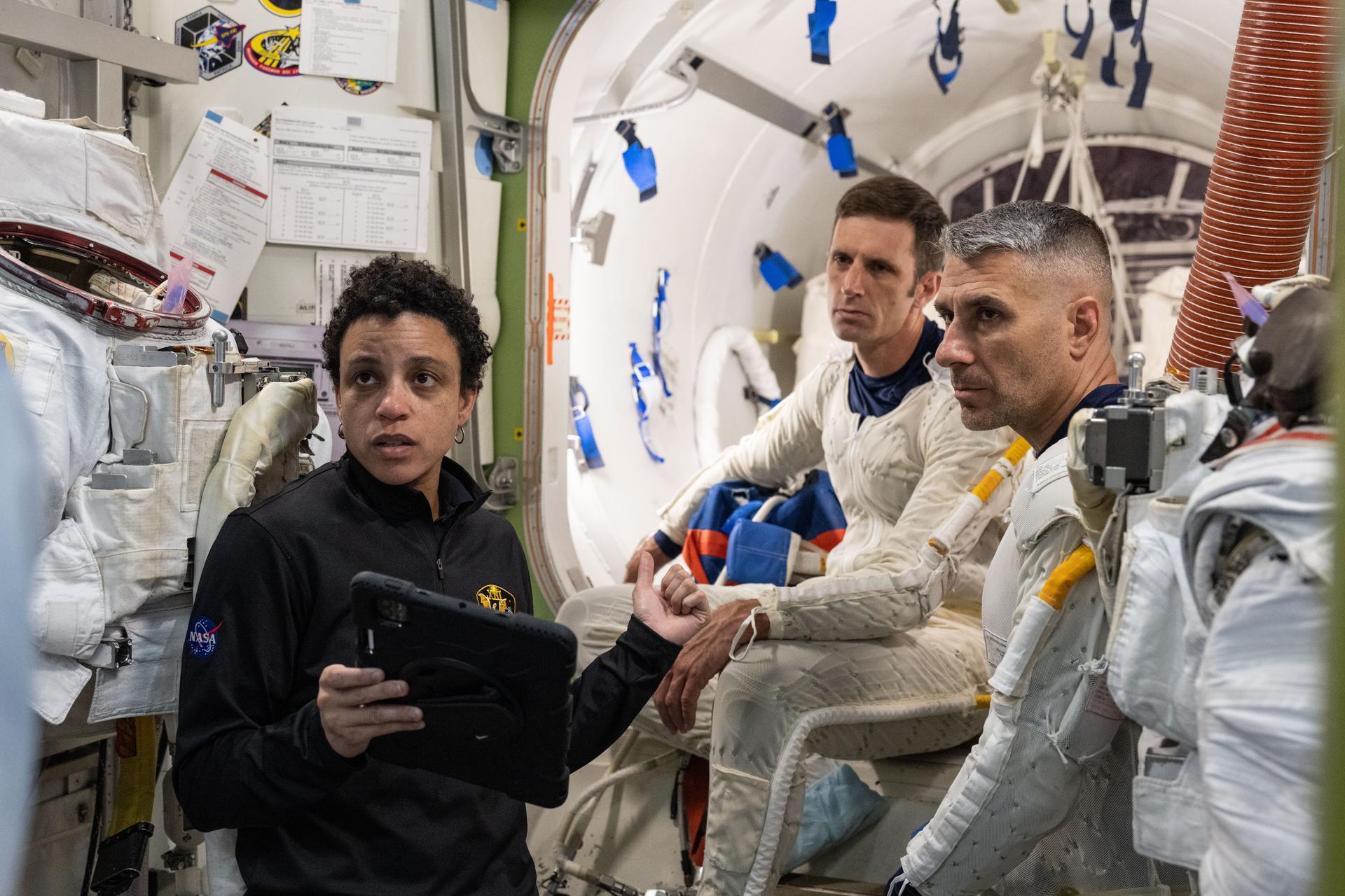 NASA astronaut Jessica Watkins (left) assists CSA (Canadian Space Agency) astronaut Josh Kutryk (background) and NASA astronaut Luke Delaney (right) as they practice suiting up in spacesuits in an International Space Station airlock simulator at Johnson Space Center’s (JSC) Space Vehicle Mockup Facility in Houston, Texas. Astronauts familiarize themselves with spacesuit systems and procedures and practice Quest airlock operations before conducting spacewalk training at JSC’s Neutral Buoyancy Laboratory in simulated microgravity.