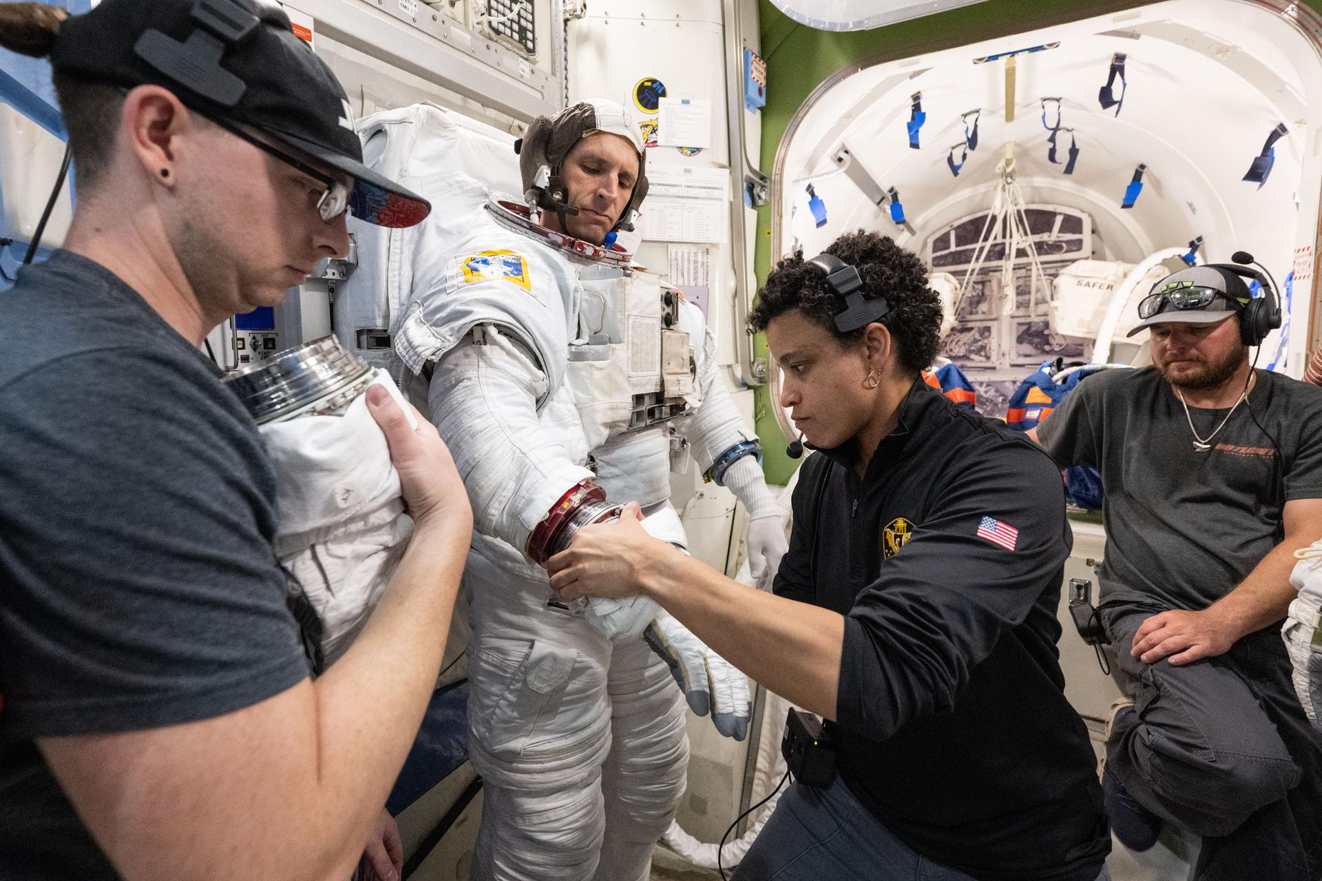 NASA astronaut Jessica Watkins (center), surrounded by training specialists, assists CSA (Canadian Space Agency) astronaut Josh Kutryk as he practices suiting up in a spacesuit in an International Space Station airlock simulator at Johnson Space Center’s (JSC) Space Vehicle Mockup Facility in Houston, Texas. Astronauts familiarize themselves with spacesuit systems and procedures and practice Quest airlock operations before conducting spacewalk training at JSC’s Neutral Buoyancy Laboratory in simulated microgravity.