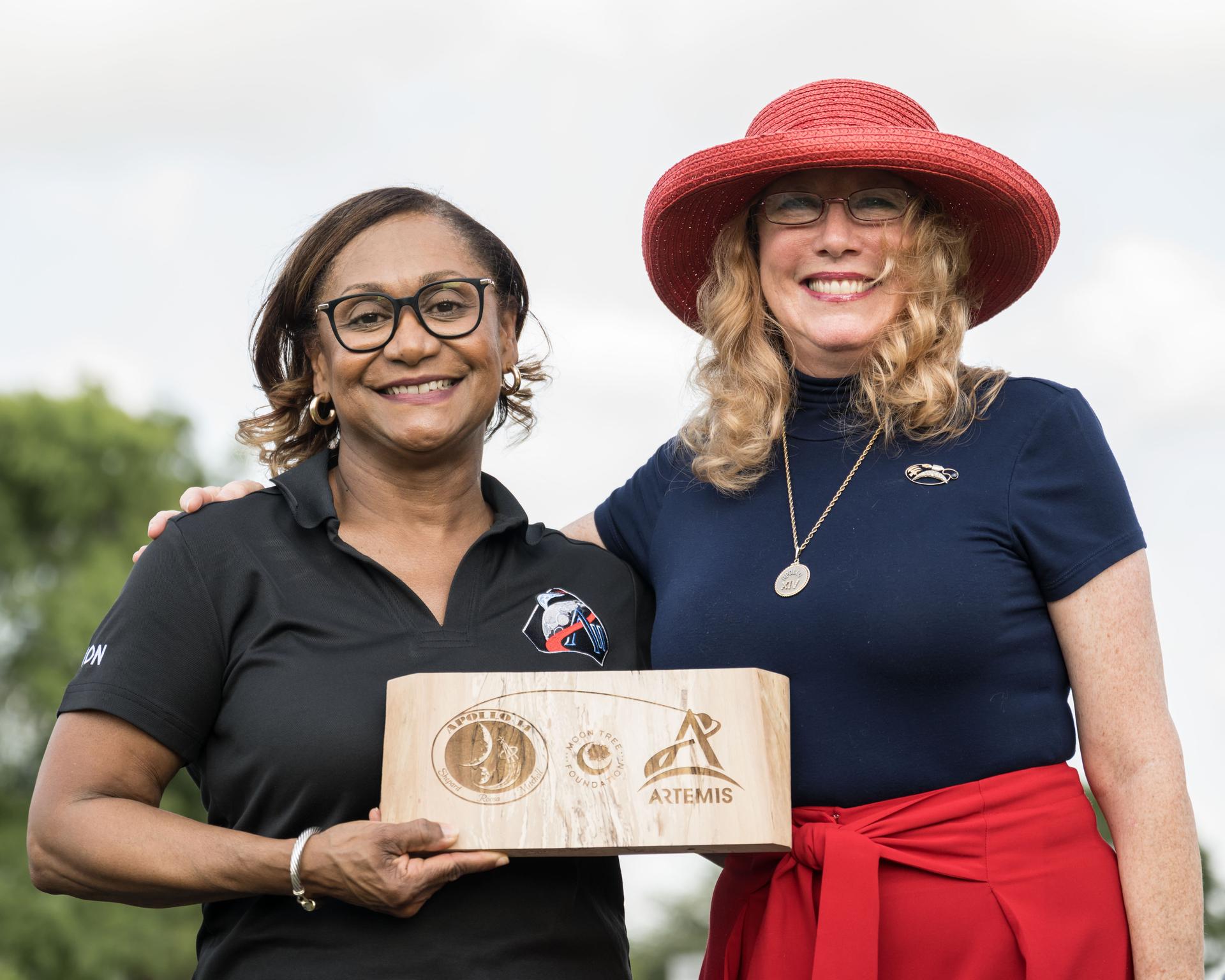 jsc2026e396742 (June 25, 2026) - NASA's Johnson Space Center Director Vanessa Wyche and Rosemary Roosa, president of The Moon Tree foundation and daughter of late Apollo 14 astronaut Stuart Roosa, share a special plaque honoring the ties between the Apollo and Artemis Programs. The plaque is constructed from an original Moon tree planted soon after the Apollo 14 mission and symbolizes the passing of the baton from Apollo to Artemis. Credit: NASA