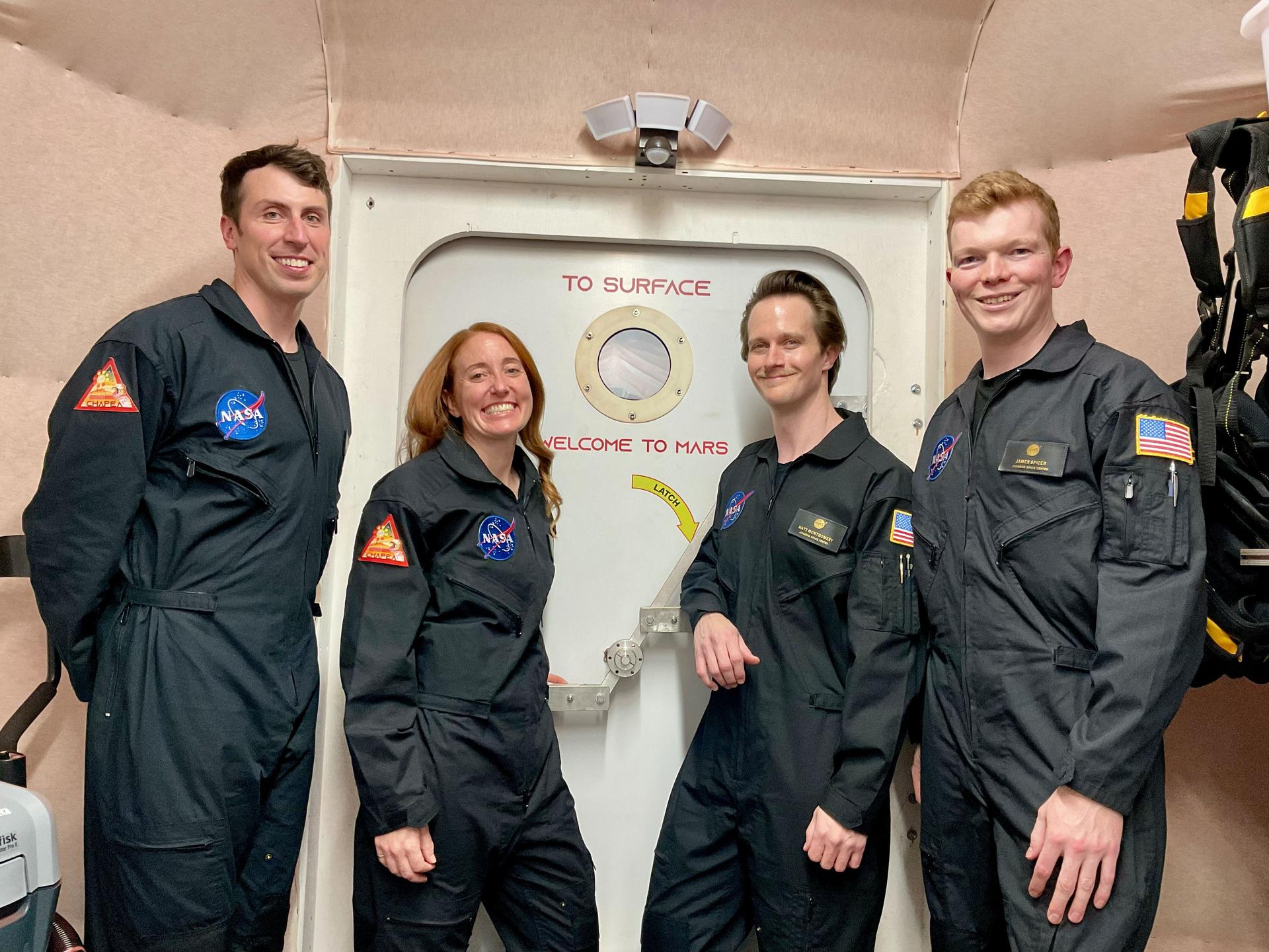 jsc2026e403153 (Nov. 24, 2025) -- CHAPEA Mission 2 crew members (from left) Ross Elder, Ellen Ellis, Matthew Montgomery, and James Spicer, pose in front of the door to the simulated Martian landscape for their first photo inside the CHAPEA habitat after their mission began in October 2025. Credit: NASA