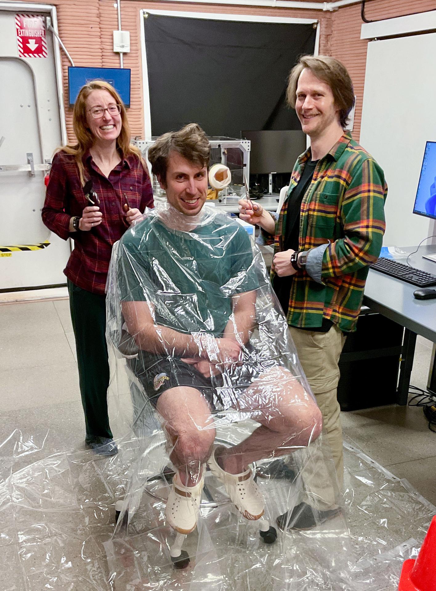 jsc2026e403160 (Jan. 11, 2026) -- Ross Elder, Crew Health and Performance Exploration Analog (CHAPEA) mission 2 commander, receiving a haircut from Ellen Ellis (left), CHAPEA mission 2 medical officer, and Matthew Montgomery (right) CHAPEA mission 2 science officer. Credit: NASA