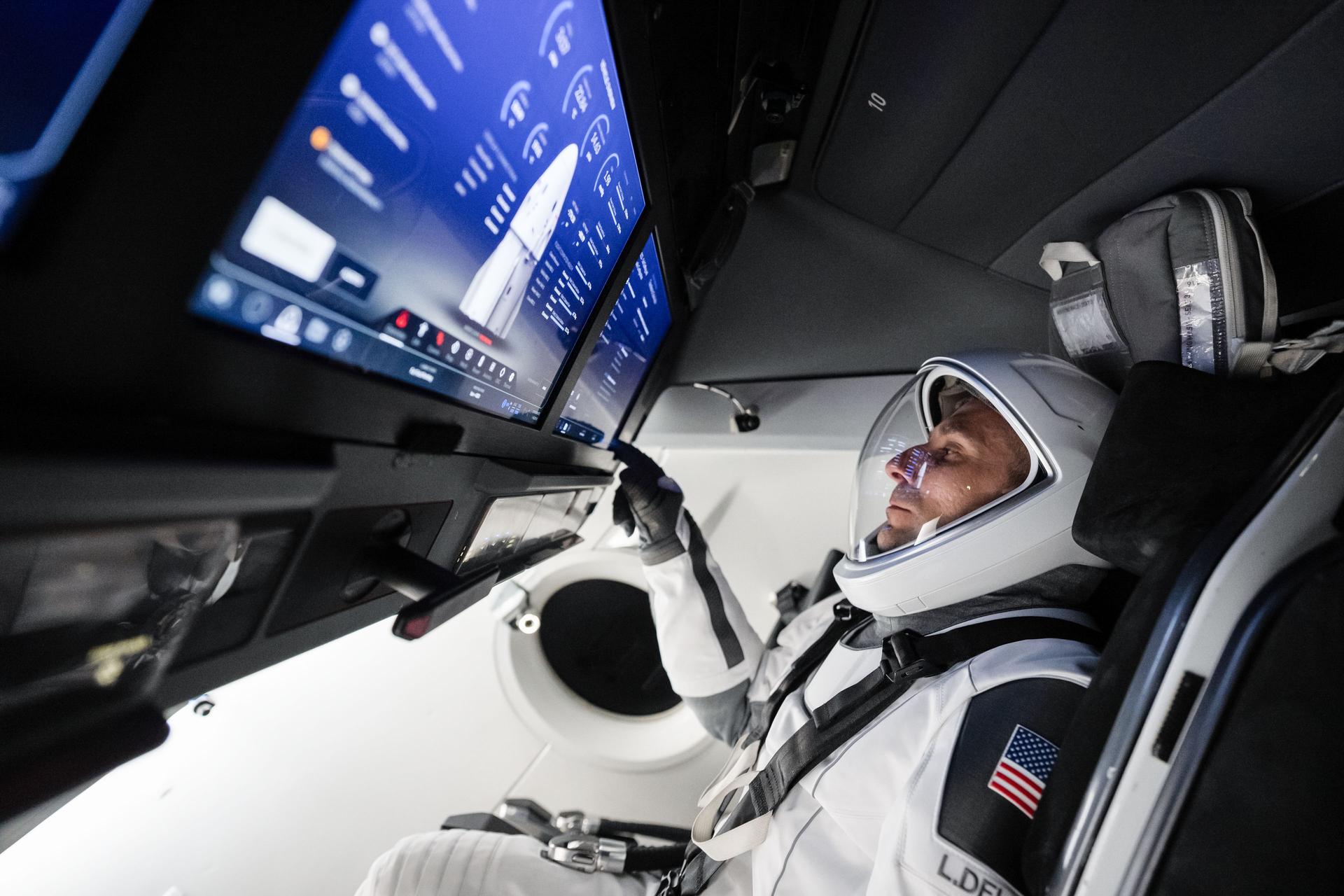NASA astronaut and SpaceX Crew‑13 Pilot Luke Delaney sits inside a Dragon spacecraft mockup while tapping a cockpit screen interface during a pre‑flight training session at SpaceX headquarters in Hawthorne, California.