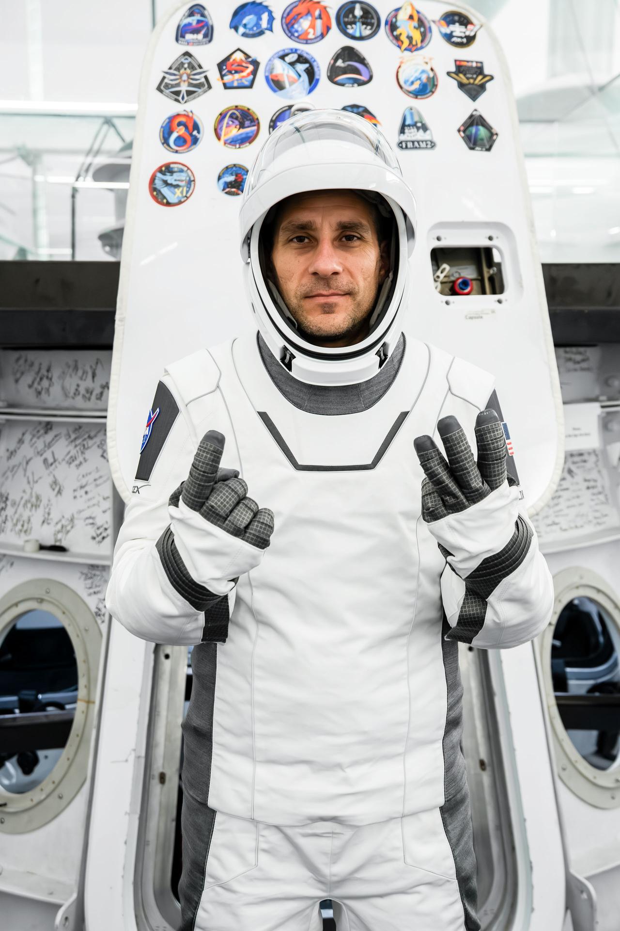 NASA astronaut and SpaceX Crew-13 Pilot Luke Delaney gestures with his fingers to show the number 13, representing his mission to the International Space Station aboard a Dragon spacecraft. Delaney poses in his pressure suit in front of a Dragon spacecraft mockup during a pre-flight training session at SpaceX headquarters in Hawthorne, California.