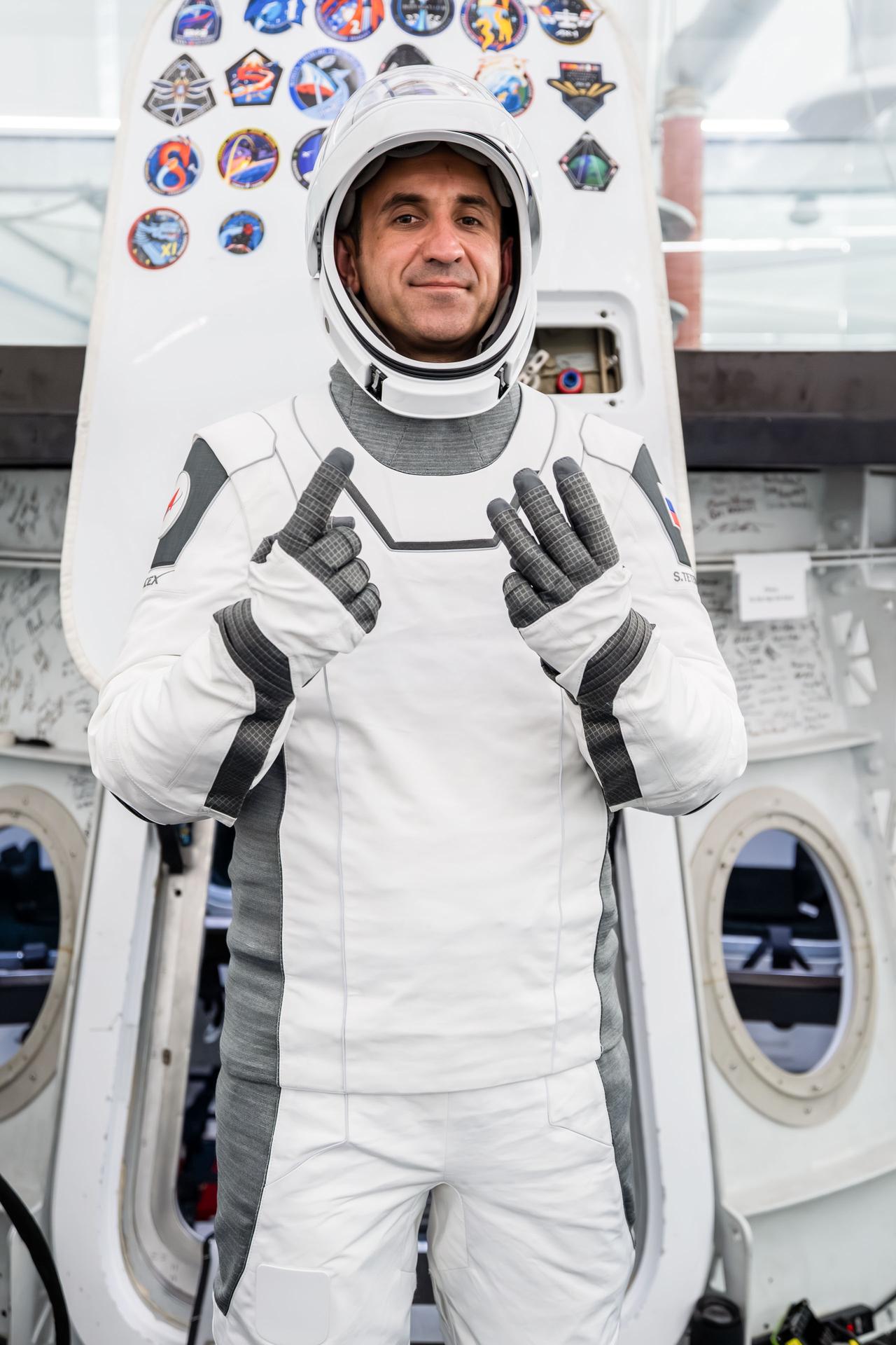 Roscosmos cosmonaut and SpaceX Crew-13 Mission Specialist Sergey Teteryatnikov gestures with his fingers to show the number 13, representing his mission to the International Space Station aboard a Dragon spacecraft. Teteryatnikov poses in his pressure suit in front of a Dragon spacecraft mockup during a pre‑flight training session at SpaceX headquarters in Hawthorne, California.