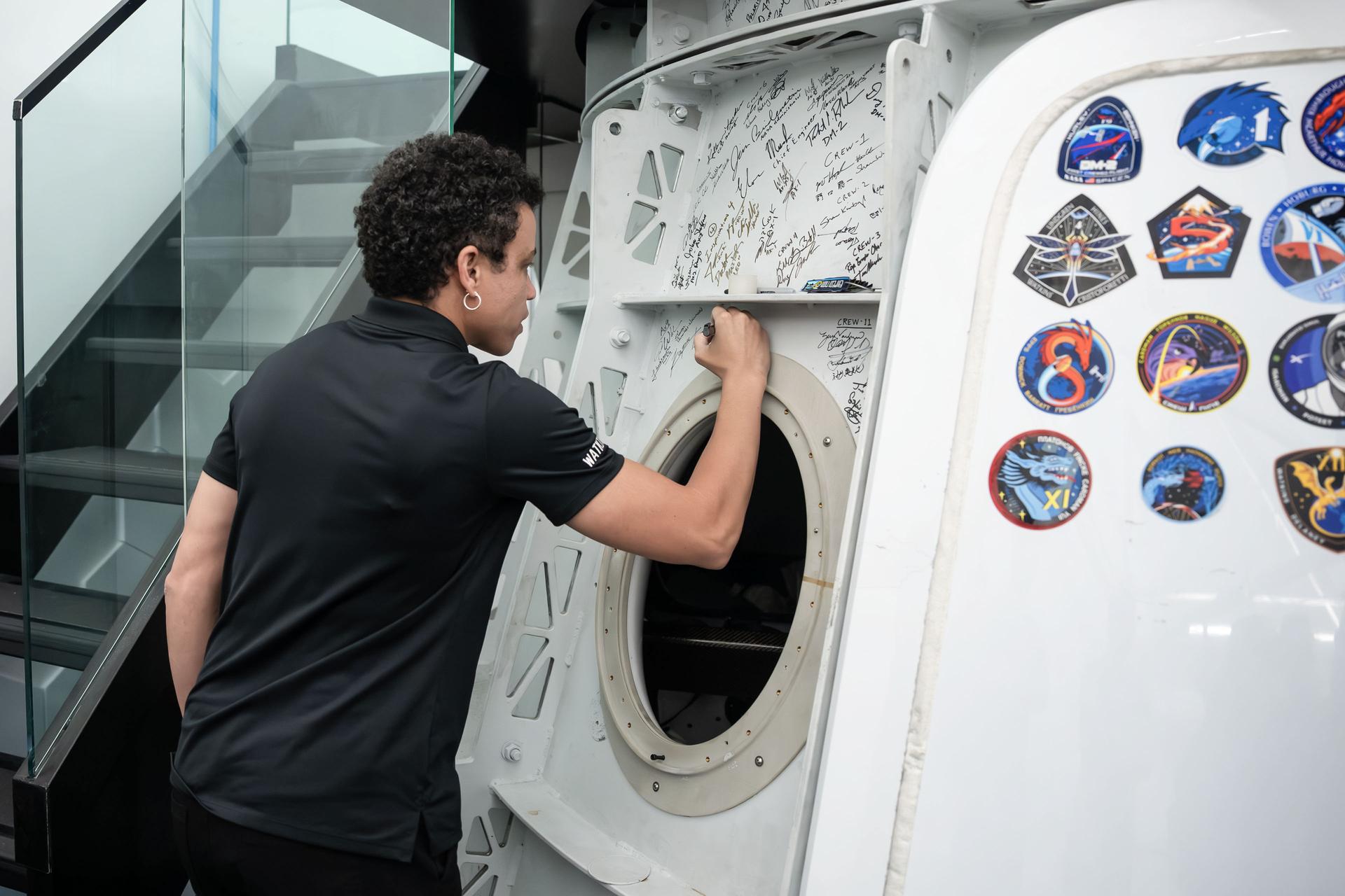 jsc2026e406104 (July 30, 3036) --- NASA astronaut and SpaceX Crew-13 Commander Jessica Watkins signs her autograph on a Dragon spacecraft mockup after completing a pre‑flight training session at SpaceX headquarters in Hawthorne, California. Credit: SpaceX