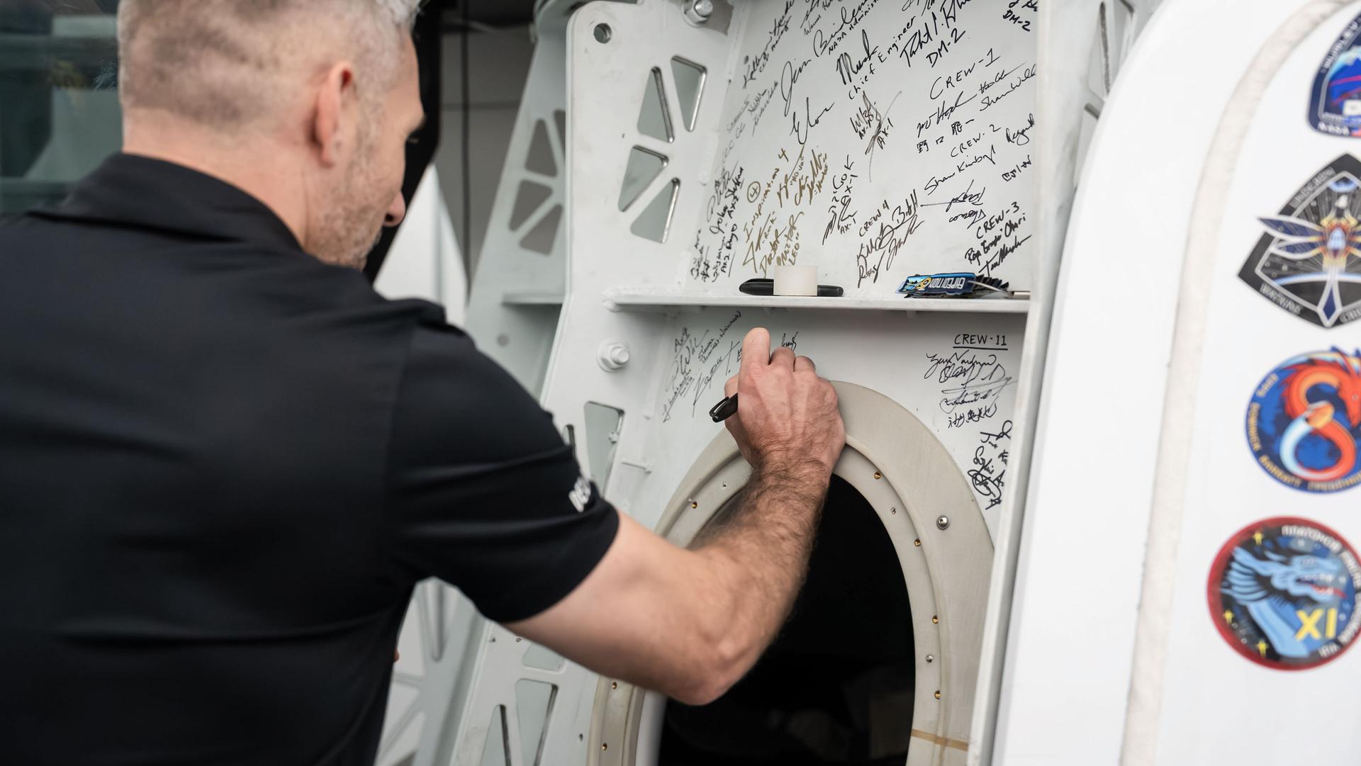 jsc2026e406105 (July 30, 3036) --- NASA astronaut and SpaceX Crew-13 Pilot Luke Delaney signs his autograph on a Dragon spacecraft mockup after completing a pre‑flight training session at SpaceX headquarters in Hawthorne, California. Credit: SpaceX
