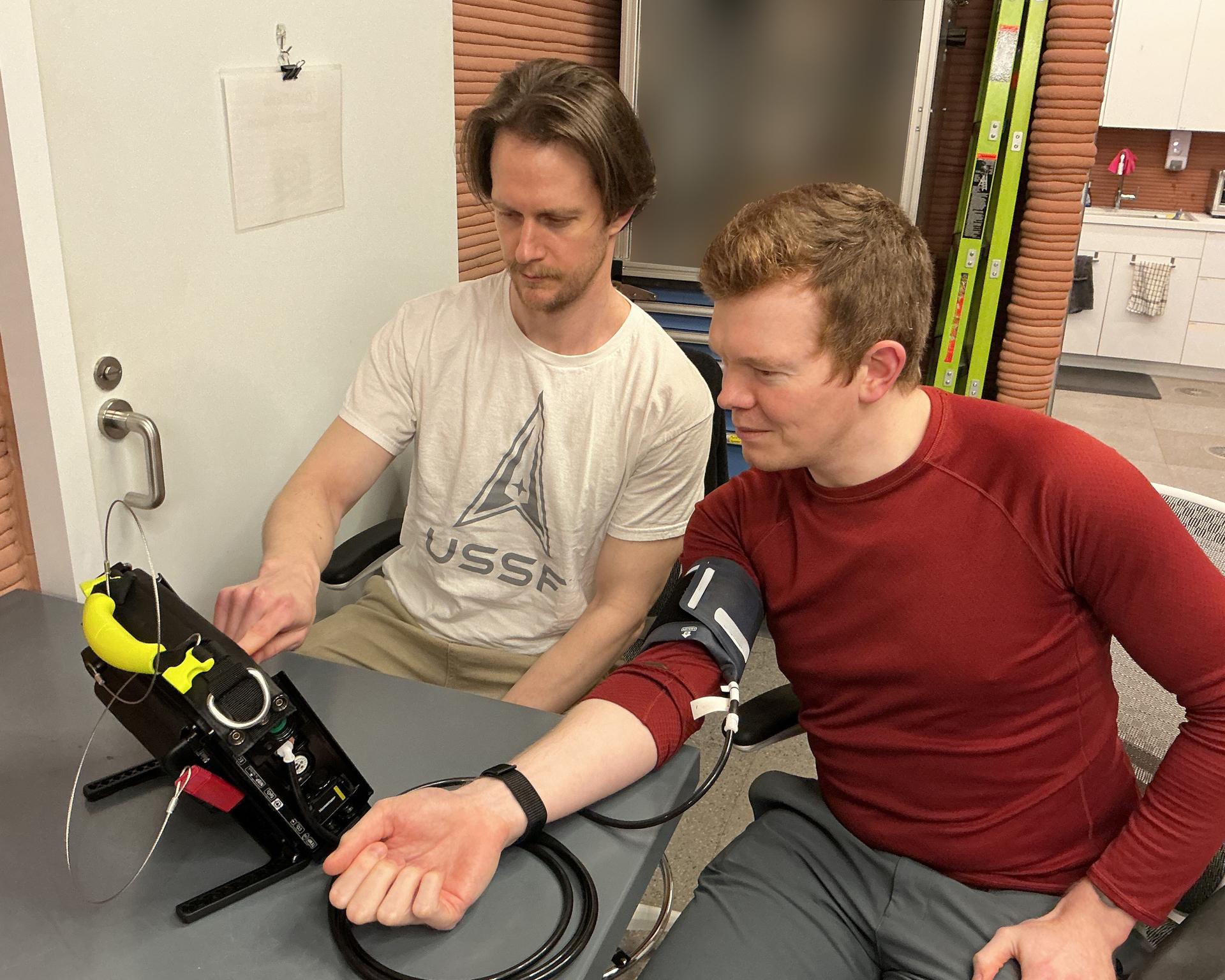 jsc2026e409154 (July 9, 2026) -- The Crew Health and Performance Exploration Analog (CHAPEA) Mission 2 crew test a specialized medical monitoring device that measures blood pressure and other health markers (from left: Matthew Montgomery, James Spicer). Credit: NASA
