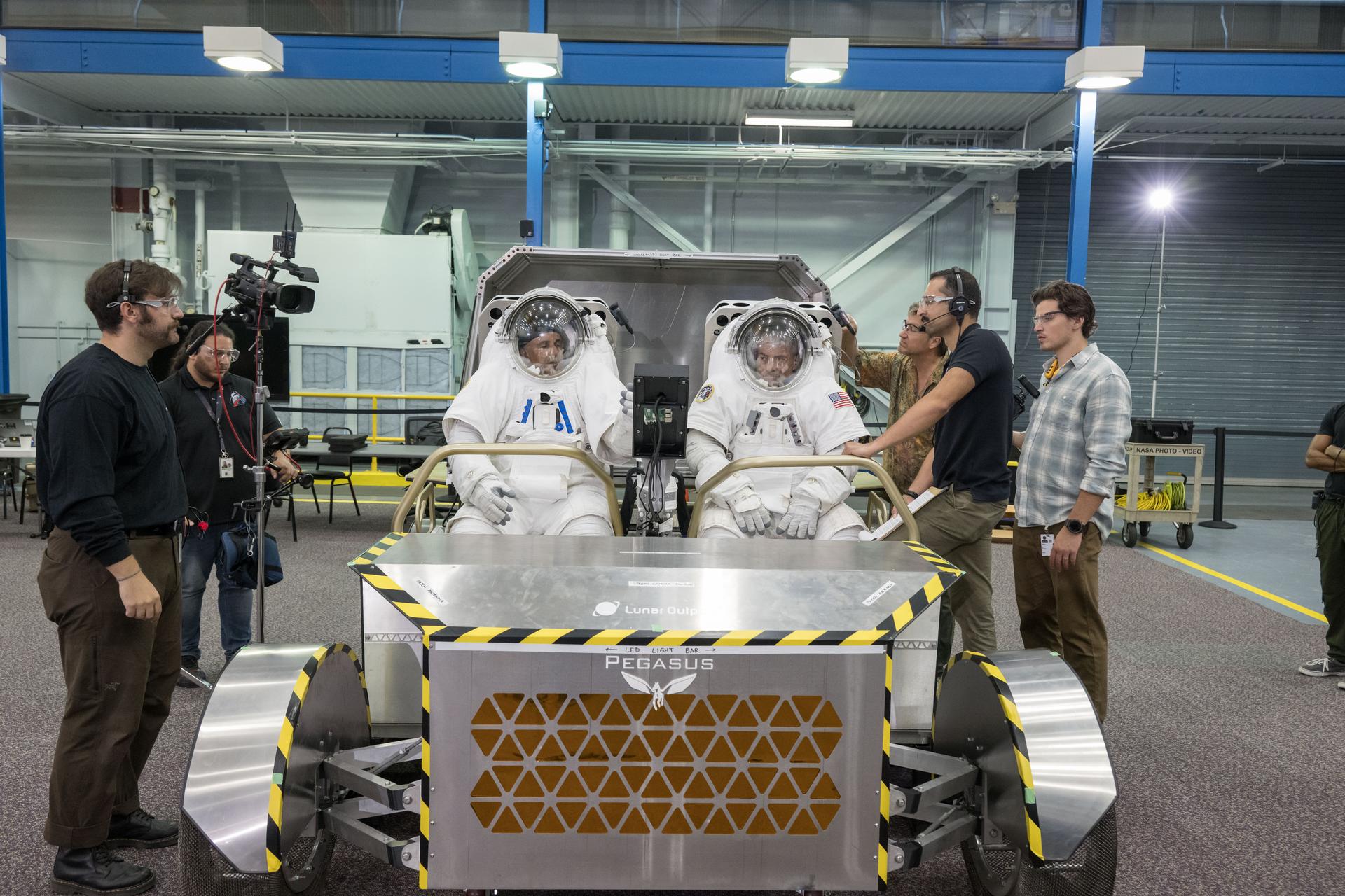 NASA astronauts Joe Acaba (left) and Mark Vande Hei (right) sit inside Lunar Outpost’s Pegasus lunar terrain vehicle prototype during human-in-the-loop testing at NASA’s Johnson Space Center where they evaluated the design, usability, and crew comfort of Lunar Outpost’s lunar rover. NASA selected Lunar Outpost and Astrolab in May 2026 to build and deliver the first phase of lunar terrain vehicles for Moon Base development. Image Credit: NASA/Bill Stafford