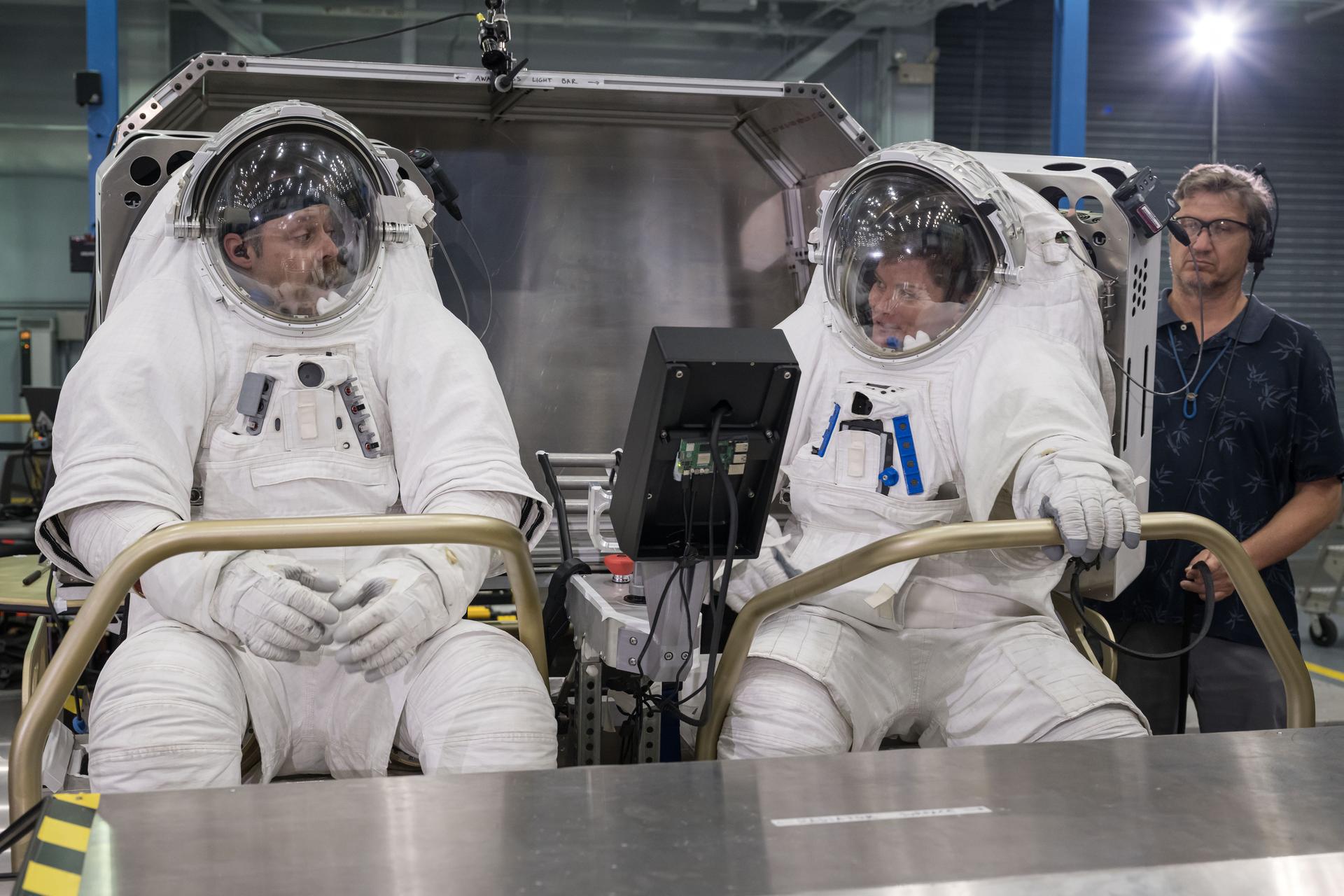 Artemis EVA training lead Scott Wray (left) and NASA astronaut Anne McClain (right) sit inside Lunar Outpost’s Pegasus lunar terrain vehicle prototype during human-in-the-loop testing at NASA’s Johnson Space Center where they evaluated the design, usability, and crew comfort of Lunar Outpost’s lunar rover. NASA selected Lunar Outpost and Astrolab in May 2026 to build and deliver the first phase of lunar terrain vehicles for Moon Base development. Image Credit: NASA/Robert Markowitz