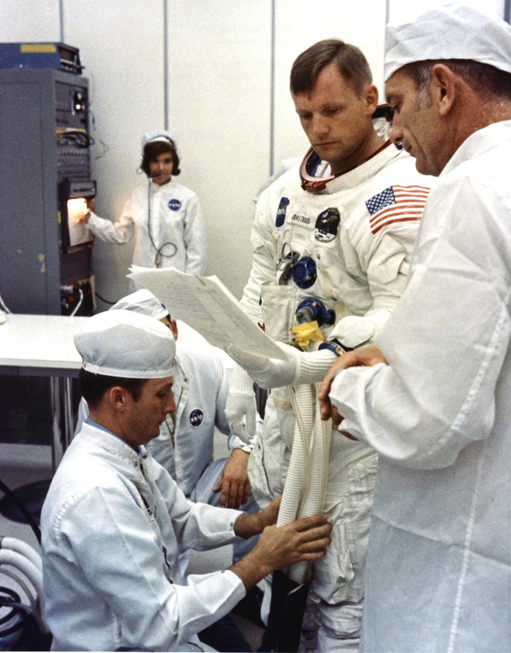 Apollo 11 Commander Neil Armstrong is looking over flight plans while being assisted by a spacesuit technician during suiting operations in the Manned Spacecraft Operations Building (MSOB) prior to the astronauts' departure to Launch Pad 39A. The three astronauts, Edwin E. Aldrin Jr., Neil A. Armstrong and Michael Collins will then board the Saturn V launch vehicle, scheduled for a 9:32 a.m. EDT liftoff, for the first manned lunar landing mission