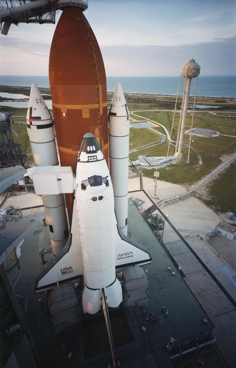 KSC-84PC-476 (For release Aug. 29, 1984) --- Orbiter Discovery is poised on Launch Pad 39A as the sun sets the evening prior to its maiden launch. Space shuttle Discovery (STS-41D) was successfully launched at 8:41 a.m. Aug. 30, 1984, after two failed attempts in June. Carrying a crew of six astronauts and three satellites, Discovery is the third in NASA?s stable of four Space Transportation System orbiters. The six-person crew includes Commander Henry Hartsfield, Pilot Michael Coats, Mission Specialists Judith Resnik, Mike Mullane and Steve Hawley and the first commercial payload specialist, Charles Walker of McDonnell Douglas. Photo credit: NASA