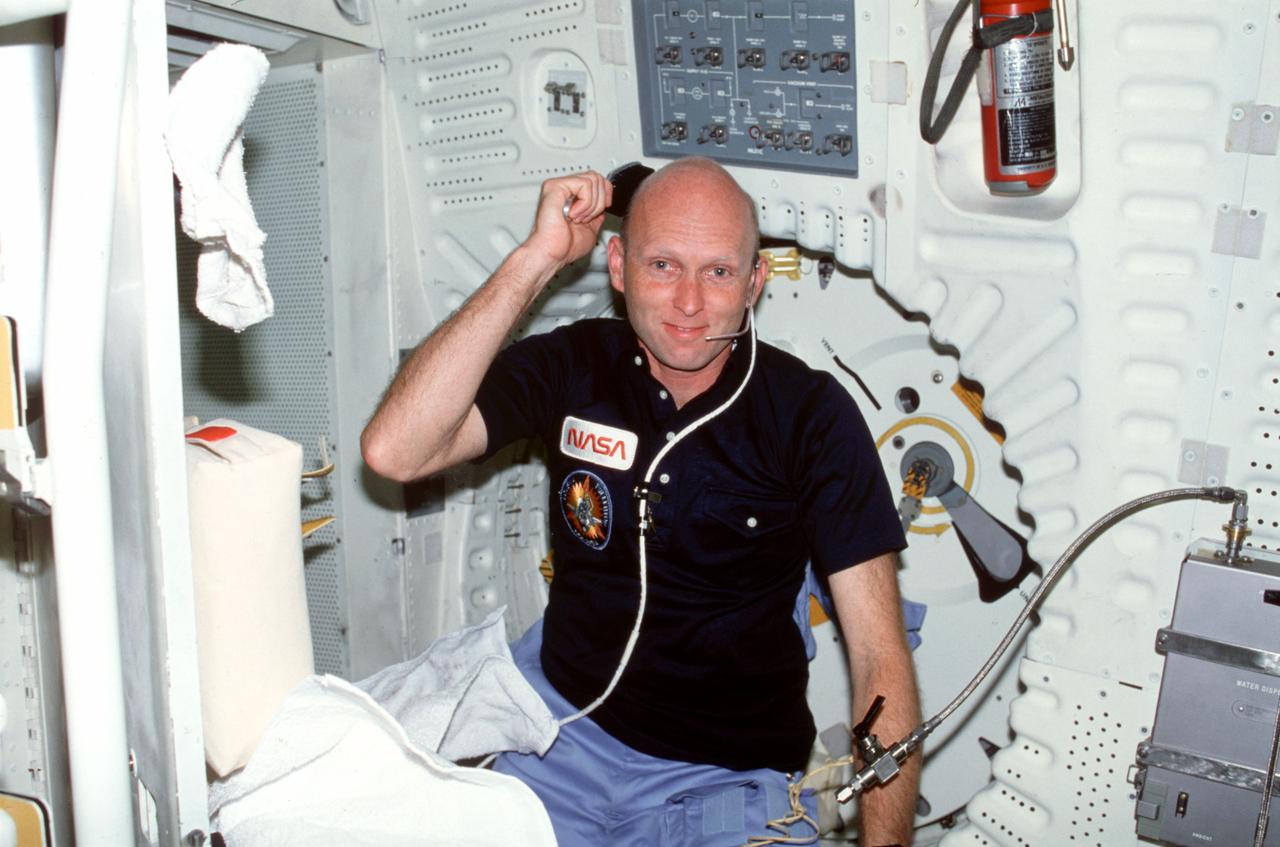 STS003-22-119 (30 March 1982) --- Astronaut Gordon Fullerton, STS-3 pilot, wearing communications kit assembly (ASSY) mini-headset (HDST), uses hygiene kit hair brush on aft middeck. He makes light of his lack of hair during a freshening up session. He makes a token effort with a hair brush. Side hatch and panel ML31C appear behind him. Photo credit: NASA