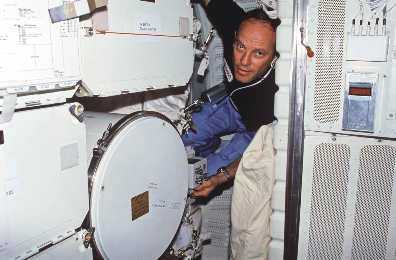 STS003-22-127 (22-30 March 1982) --- Astronaut Jack R. Lousma, STS-3 commander, wearing communications kit assembly (assy) mini-headset, adjusts controls on Monodisperse Latex Reactor (MLR) experiment located in forward middeck lockers MF57H and MF57K. To reach MLR support electronics assy controls, Lousma squeezes in between forward lockers and Development Flight Instrument (DFI) unit on starboard bulkhead. Photo credit: NASA