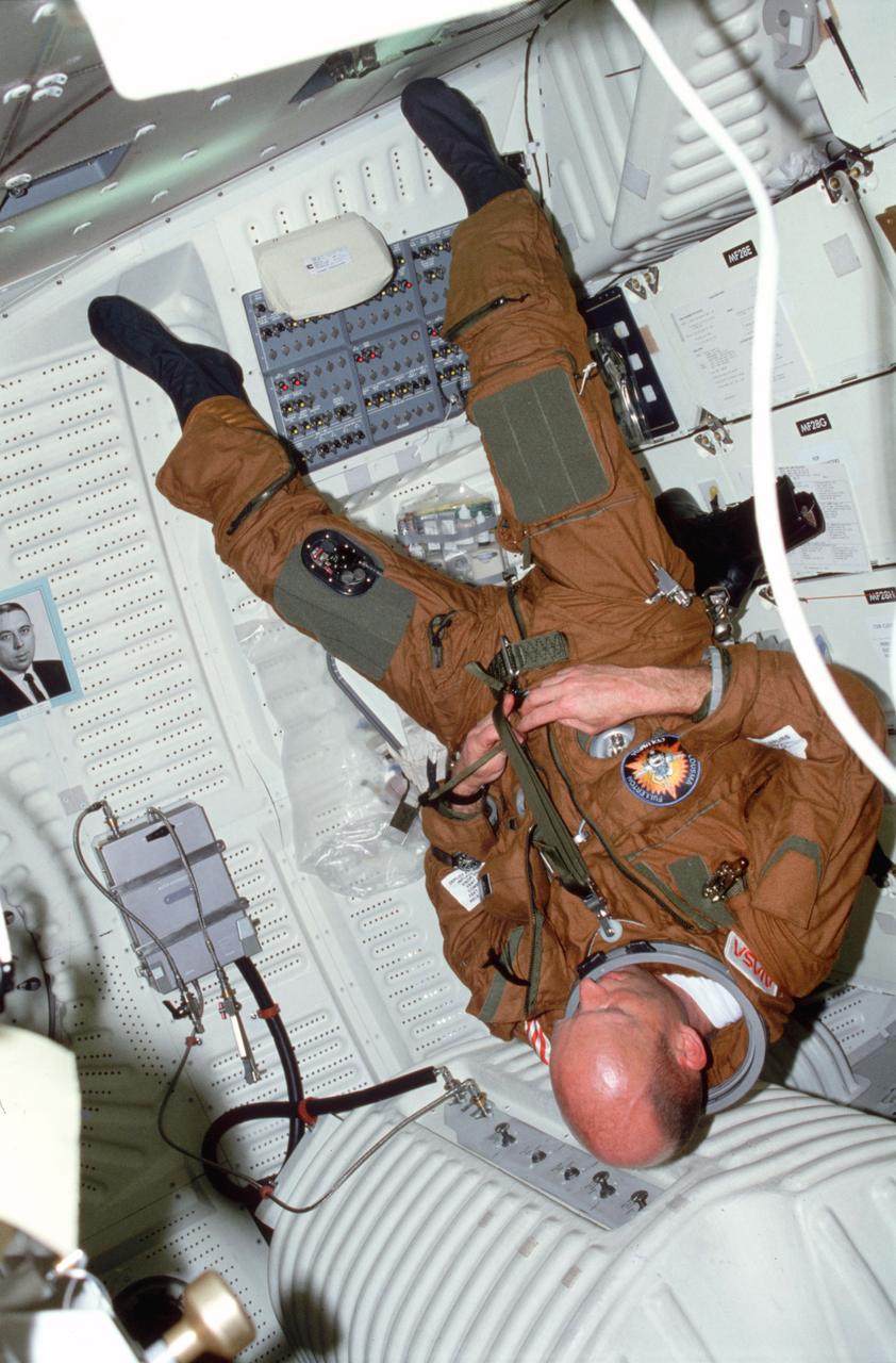 STS003-23-165 (22-30 March 1982) --- Astronaut Gordon Fullerton, STS-3 pilot, dons ejection escape suit (EES) (high altitude pressure garment) life preserver unit (LPU) on forward port side of middeck above potable water tank. Fullerton also adjusts lapbelt fitting and helmet holddown strap. Photo credit: NASA