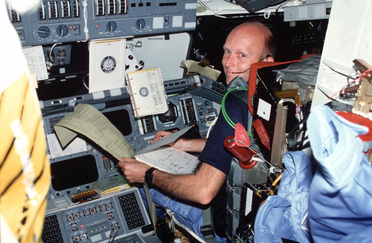 STS003-23-180 (22-30 March 1982) --- Astronaut Gordon Fullerton, STS-3 pilot, wearing communications kit assembly (ASSY) mini-headset (HDST), reviews flight data file (FDF) checklist and text and graphics system (TAGS) printout (ticker tape) while in pilots ejection seat (S2). Pilot station control panels F4, F7, F8, O3, window shade, and portable oxygen system (POS) assy appear in view. Photo credit: NASA