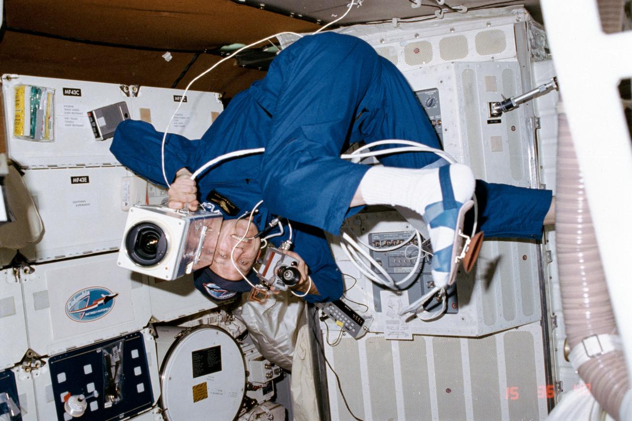 STS004-23-131 (27 June-4 July 1982) ---Astronaut Thomas K. Mattingly II, STS-4 commander, floats in the middeck area of the Earth-orbiting space shuttle Columbia. He handles two cameras at one time. In the commander’s right hand is a 16mm data acquisition camera (DAC), and in his left hand is a TV camera. Note the suction-cup equipped footwear which Mattingly revealed to the world via TV on one of his popular “cook’s tours” from crewmate Henry W. Hartsfield, pilot, operated a 35mm camera to expose this frame. Photo credit: NASA