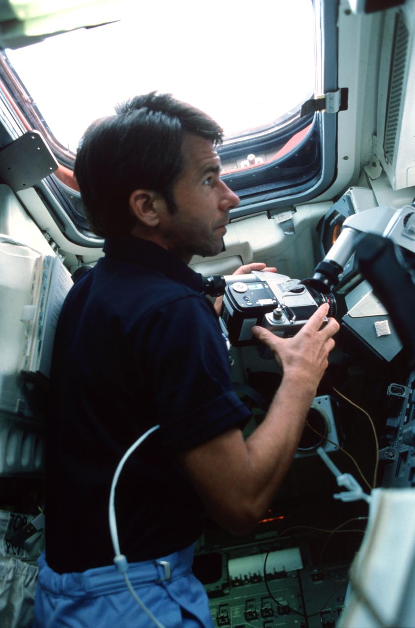 STS005-03-110 (11-16 Nov. 1982) --- Astronaut William B. Lenoir, STS-5 mission specialist, holding a 70mm HASSELBLAD camera, observes scenery through viewing window on aft flight deck on orbit station. Window W7 appears overhead. Lenoir prepares to shoot Earth-looking scenes through window above his head. Photo credit: NASA