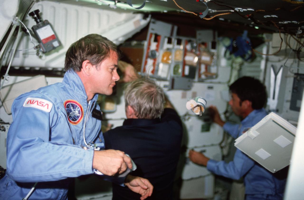 STS005-06-206 (11-16 Nov. 1982) --- Astronaut Joseph P. Allen, STS-5 mission specialist, watches a can of food and a notebook drift on the middeck as Vance C. Brand, commander, (left) and William B. Lenoir, mission specialist, (far left) work at forward middeck lockers. Photo credit: NASA