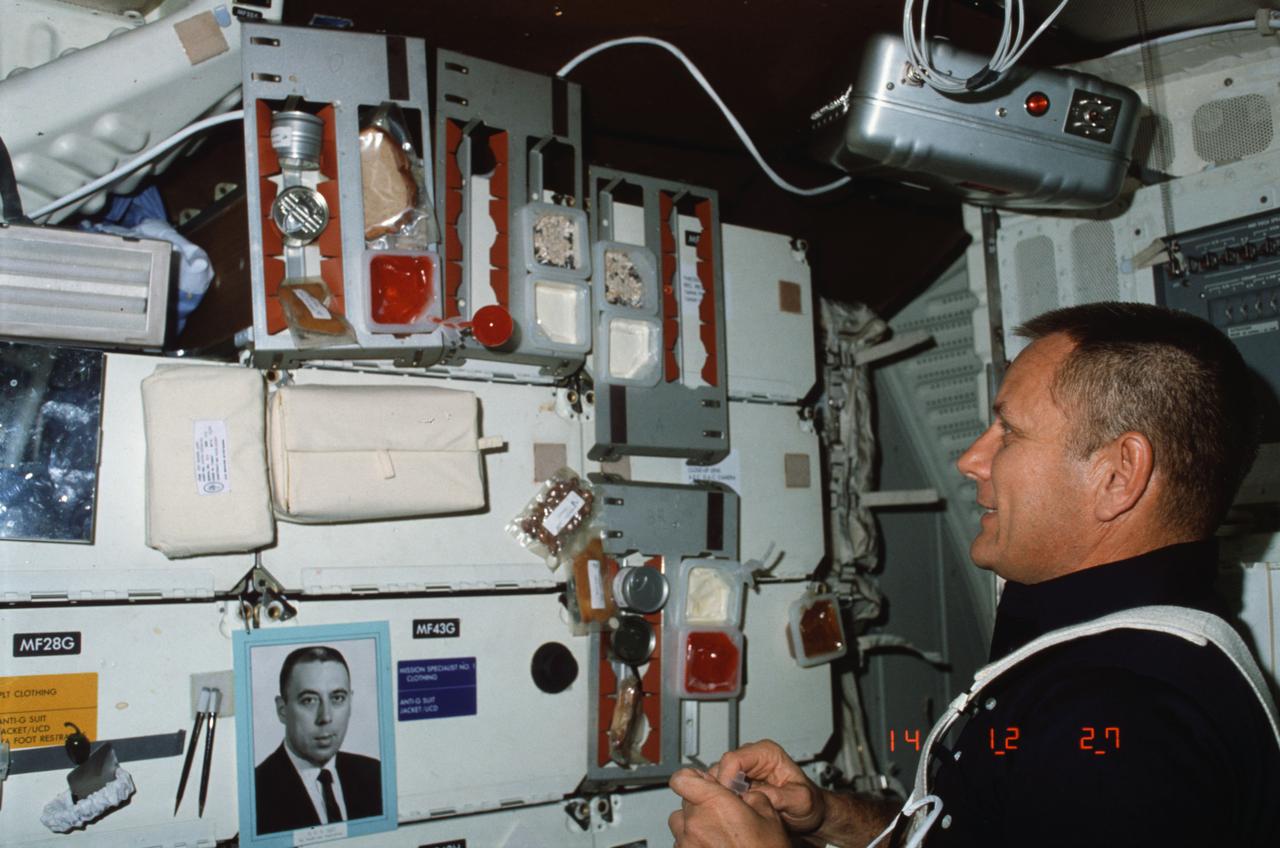 STS005-07-255 (19 Nov. 1982) --- Astronaut Robert F. Overmyer, STS-5 pilot, using beverage container and drinking straw secured in meal tray assembly (ASSY), experiments with microgravity characteristics of liquid on middeck in front of forward lockers. Overmyer also looks over packages of food attached to middeck lockers in meal tray assemblies. Carry-on food warmer appears overhead and other meal tray assemblies, personal hygiene mirror assembly, personal hygiene kit, and portrait of G.W.S. Abbey, Johnson Space Center's (JSC) Director of Flight Operations, appear on lockers. Photo credit: NASA