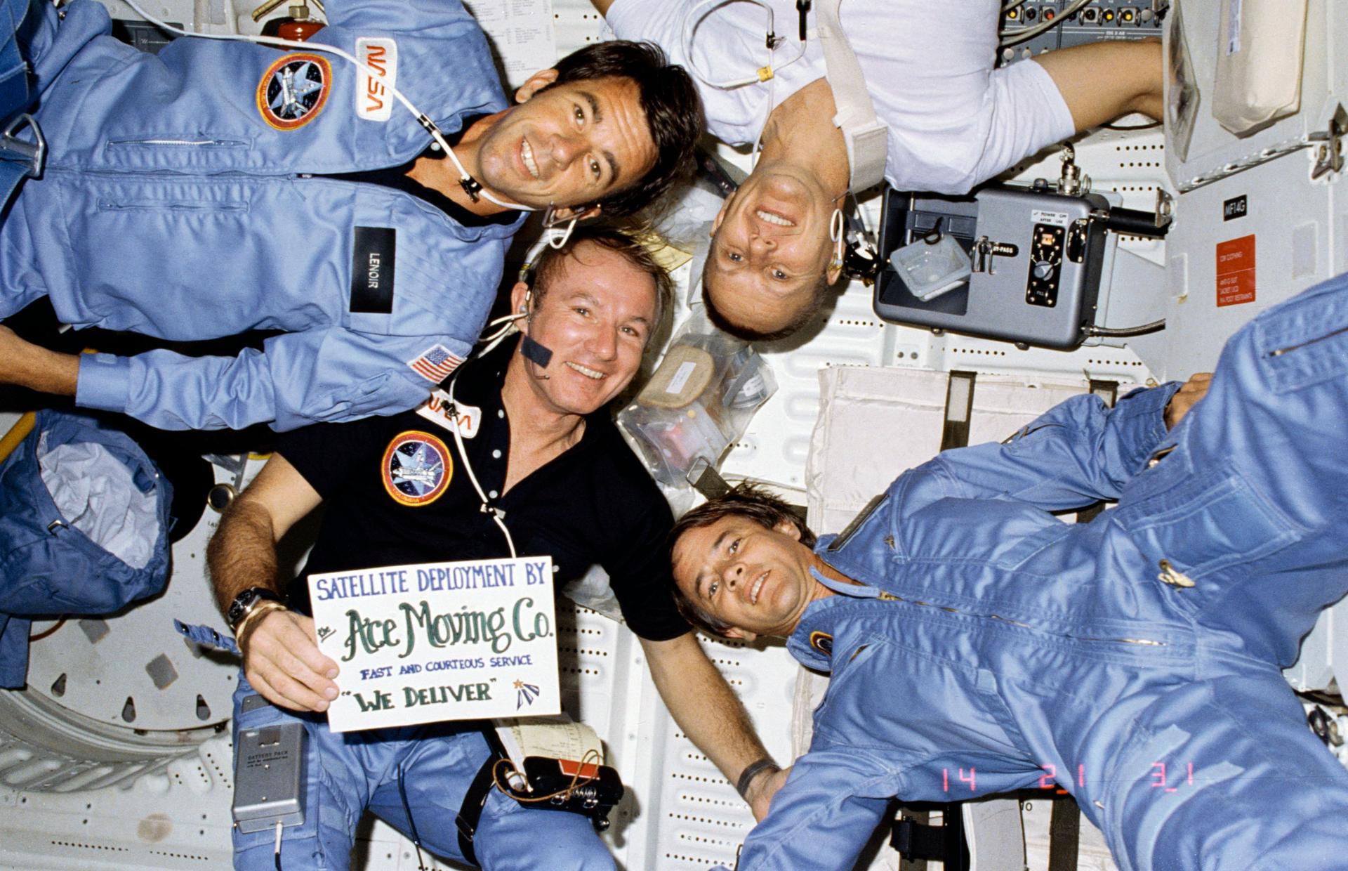 The crew of STS-5 poses for a group shot. Commander Vance Brand holds a sign that says "Ace Moving Co."